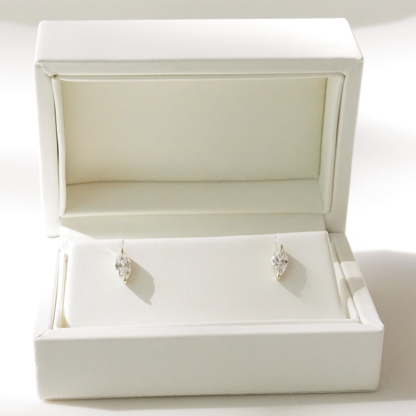 Pair of marquise diamond earrings in an open white jewelry box on a white background