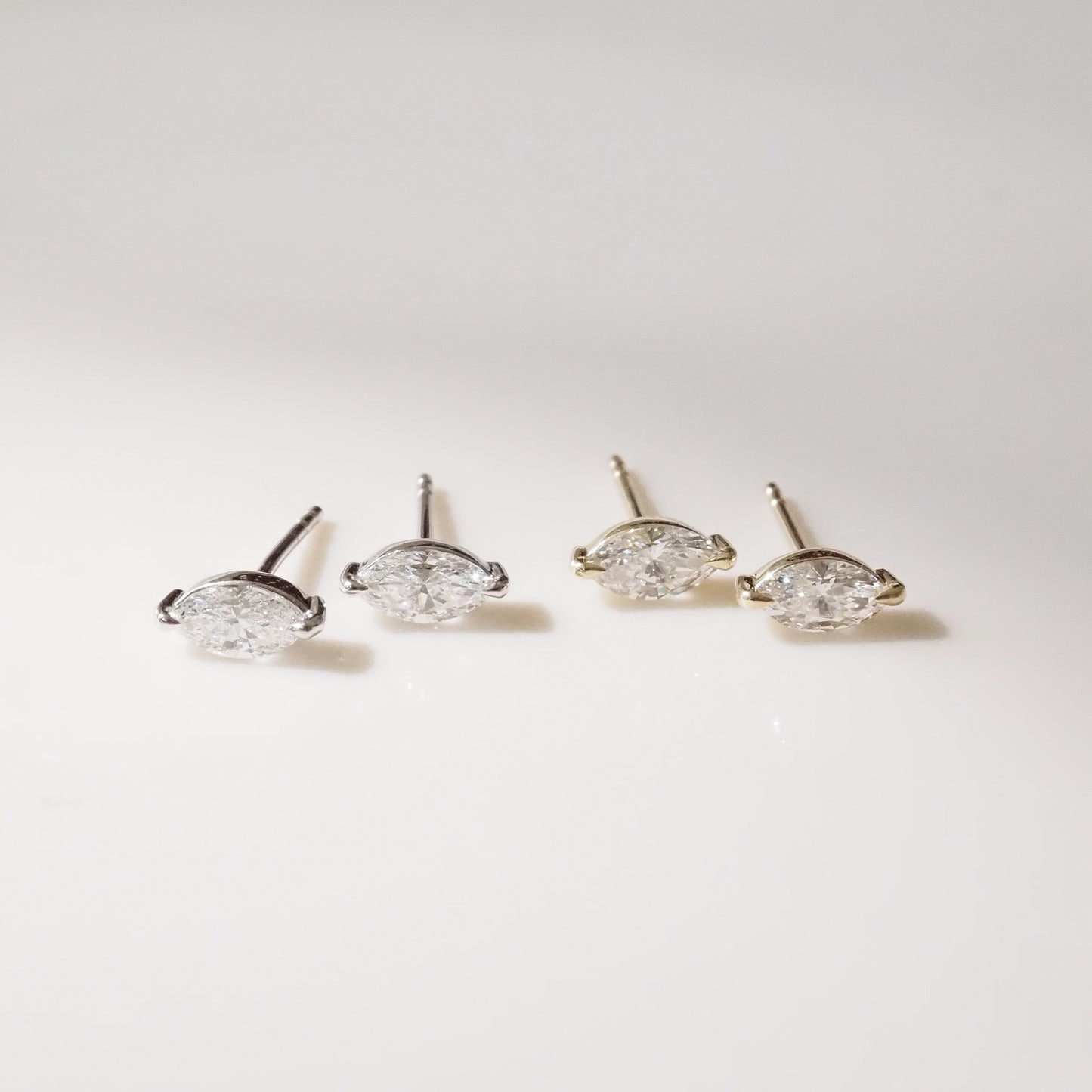 Two pairs of marquise diamond stud earrings on a light gray background