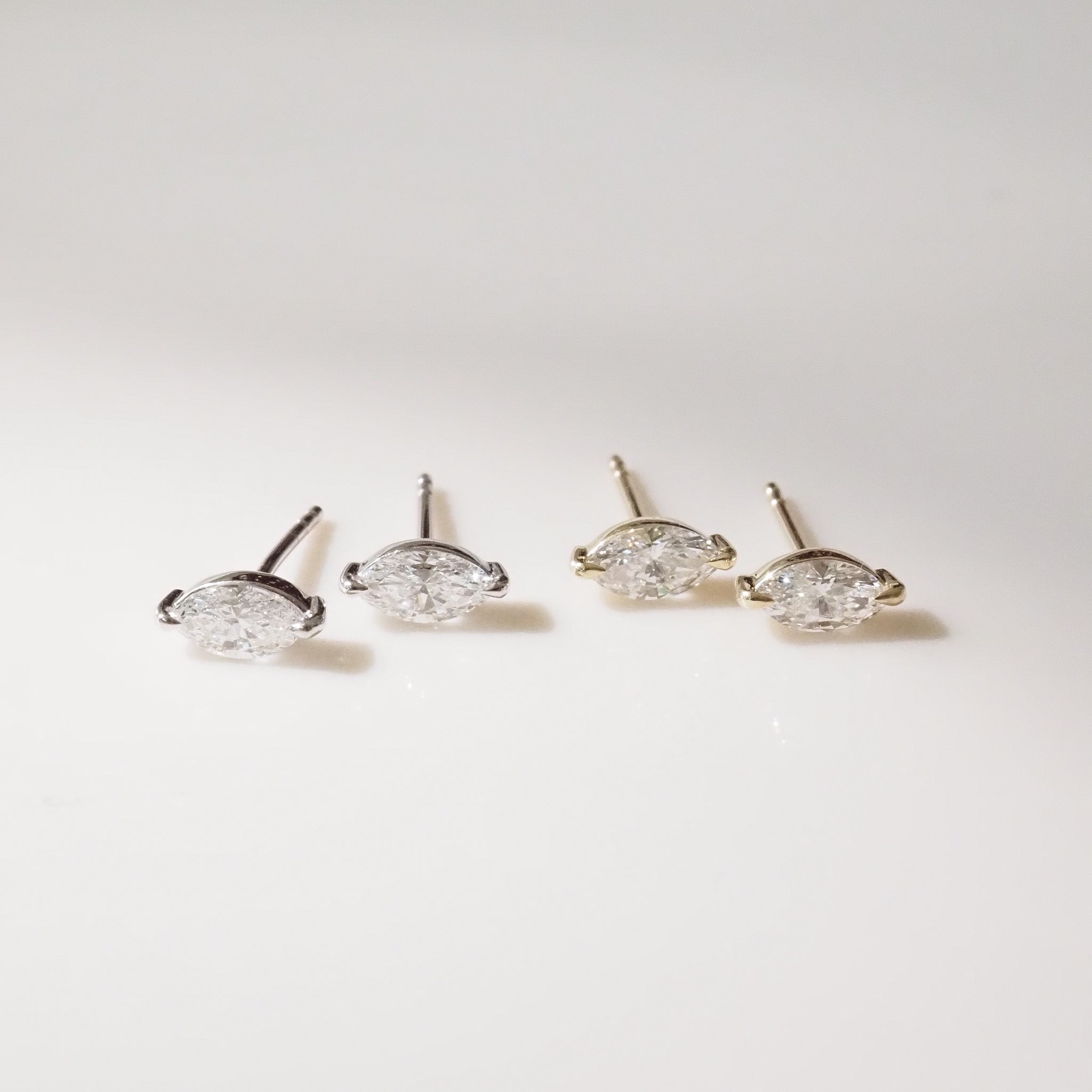 Two pairs of marquise diamond stud earrings on a light gray background