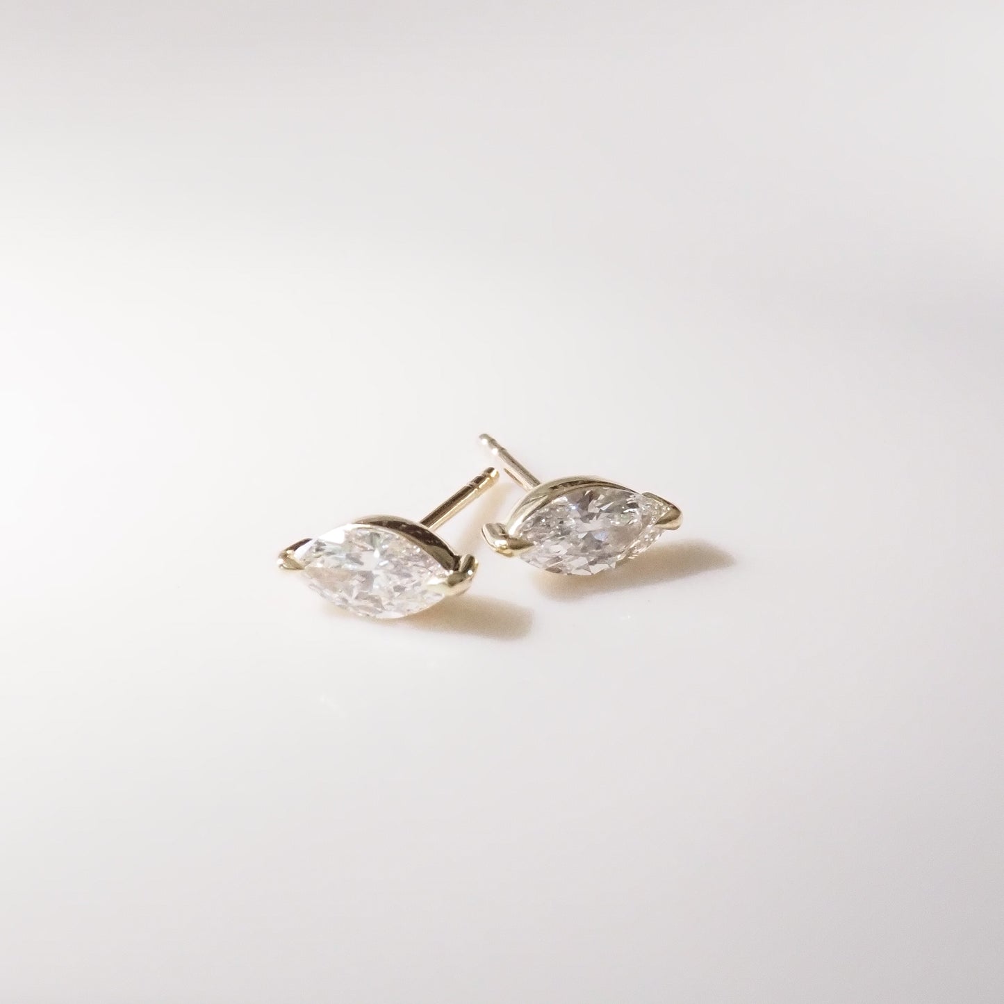 Pair of gold marquise earrings with clear gemstones on a light gray background