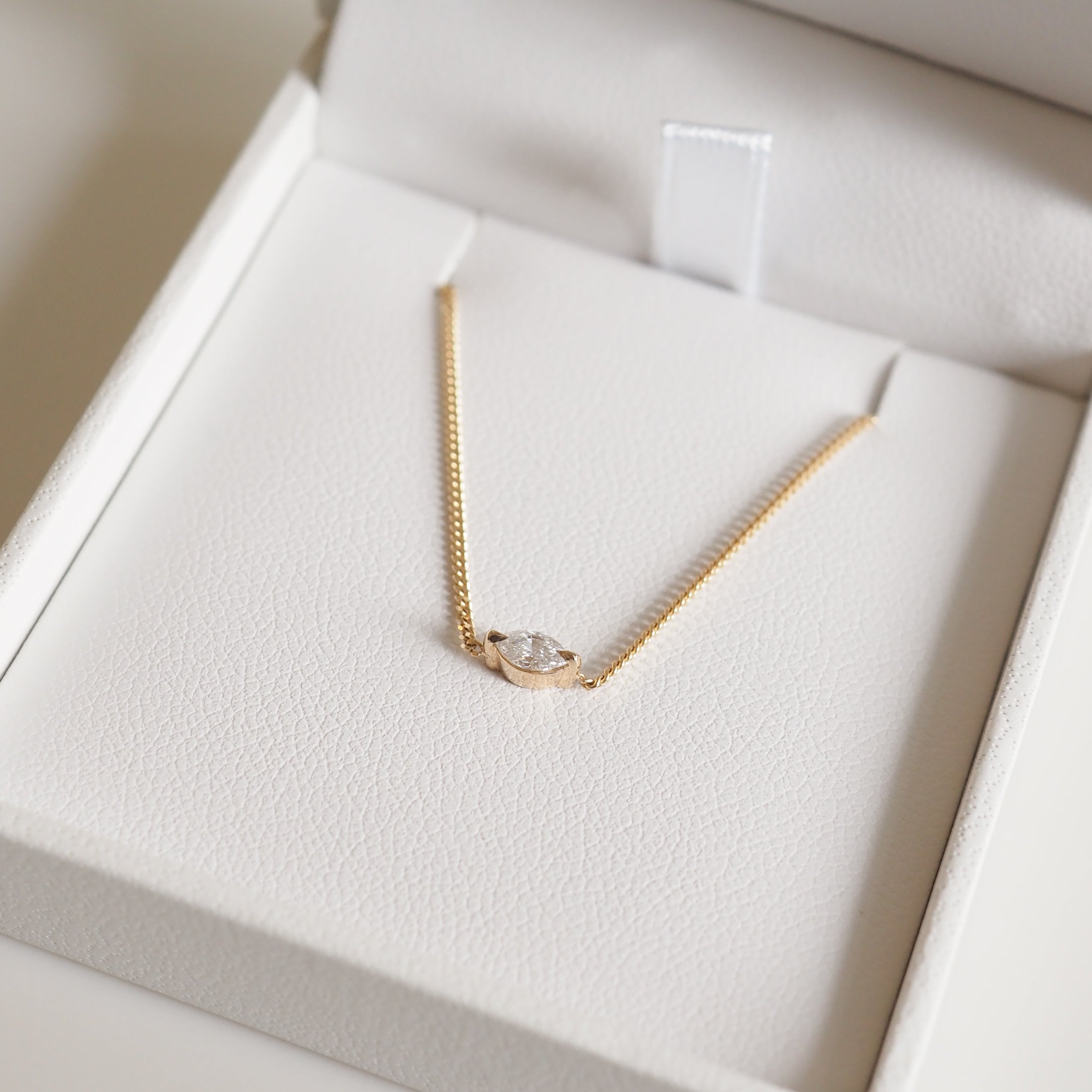 Gold necklace with a pear-shaped diamond pendant in an elegant white jewellery box, showcasing luxury and sophistication.