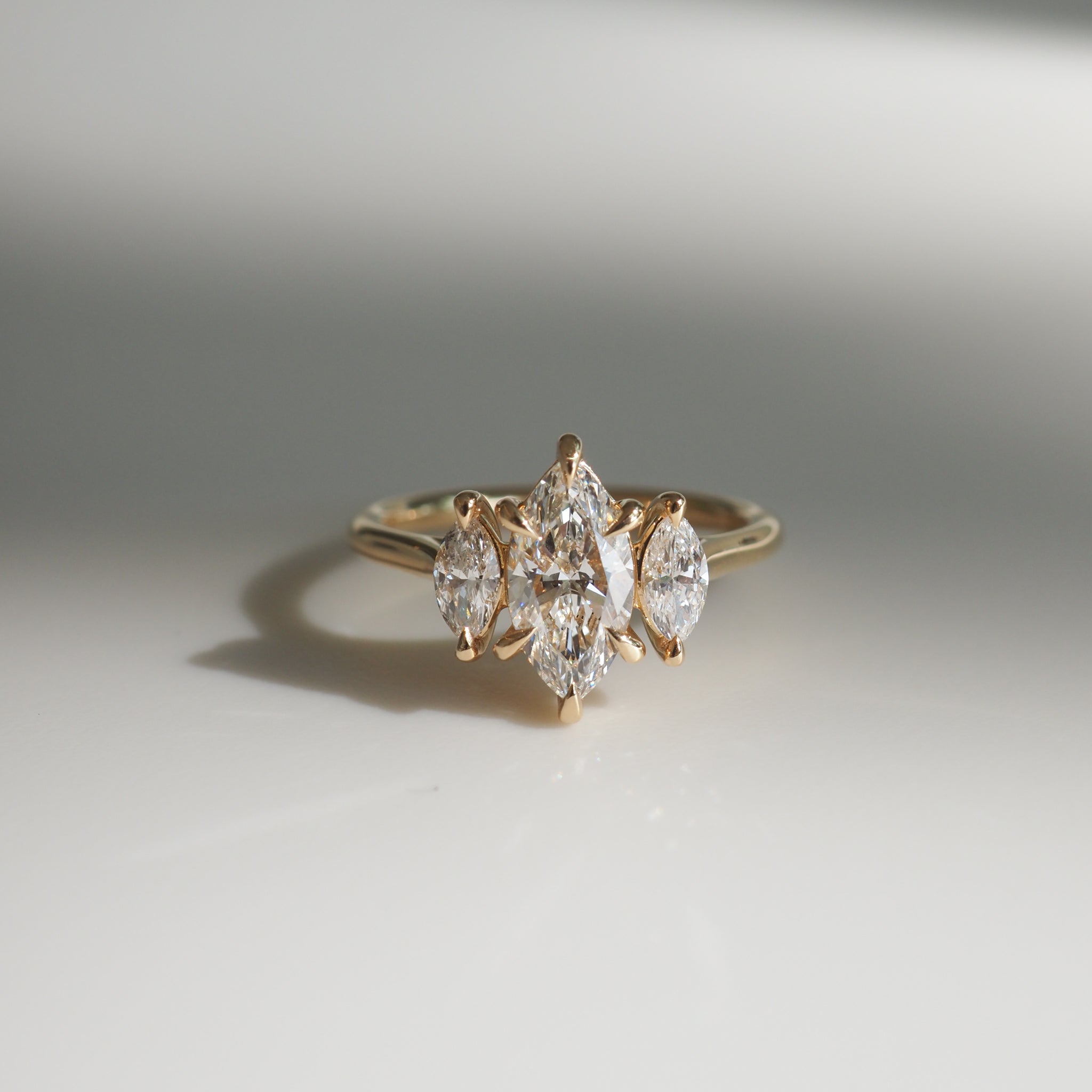 Gold ring with marquise-cut diamonds in a tri-stone setting on a reflective surface, highlighting luxury jewellery design.