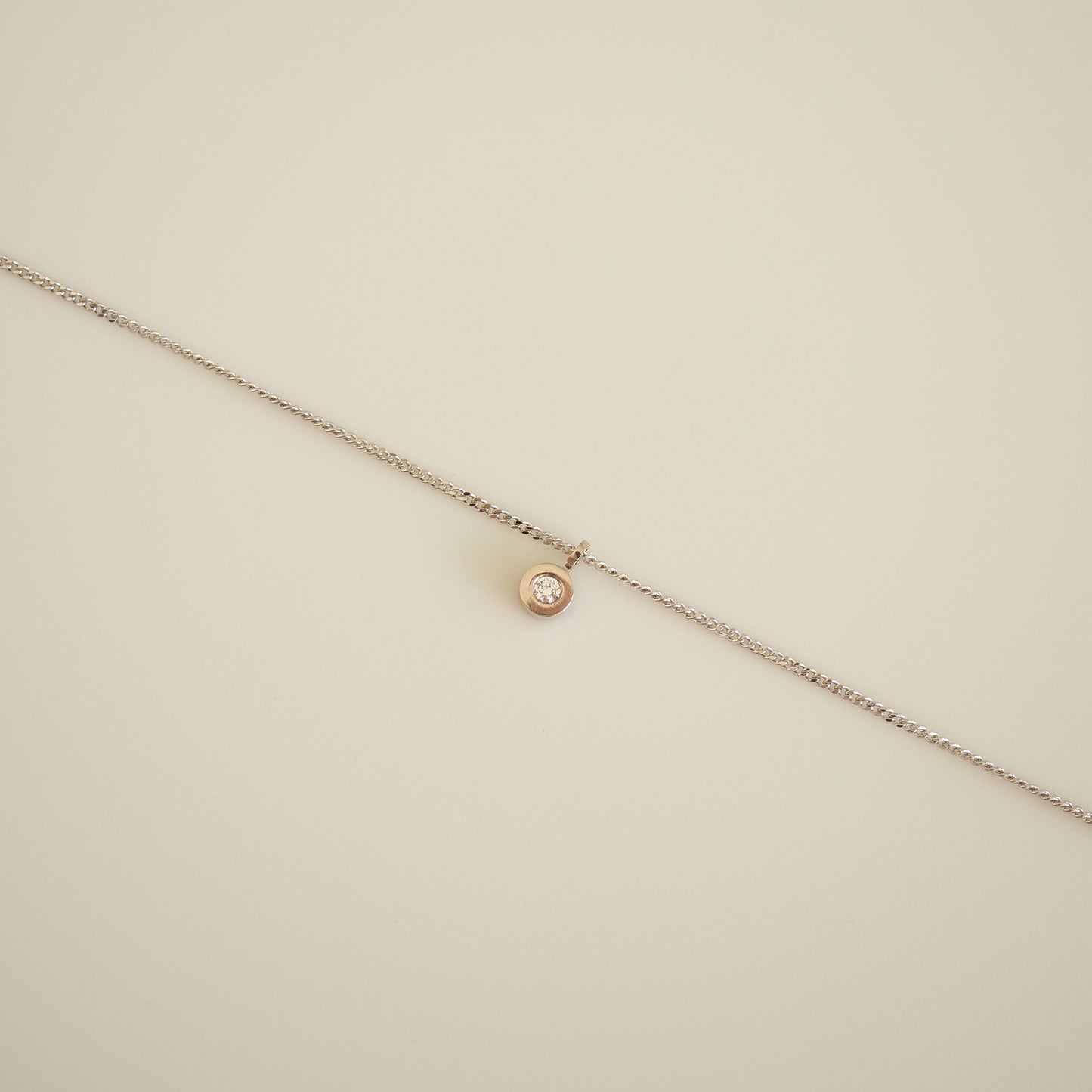 Delicate gold necklace with a round diamond pendant on a light background; luxury jewellery piece.