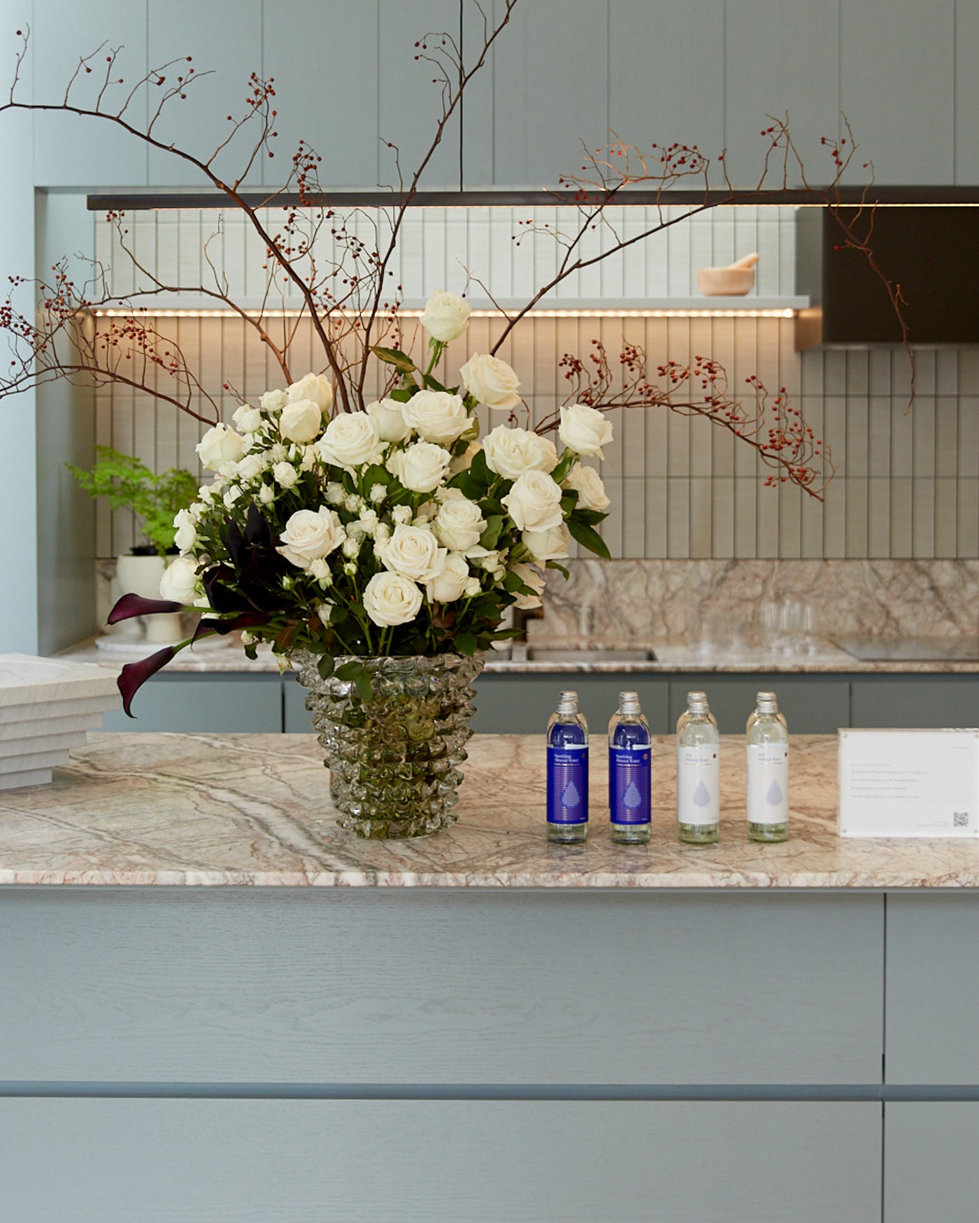 Luxurious jewellery store counter with a marble finish, featuring a vase of white roses, elegant decor, and bottled water on display.