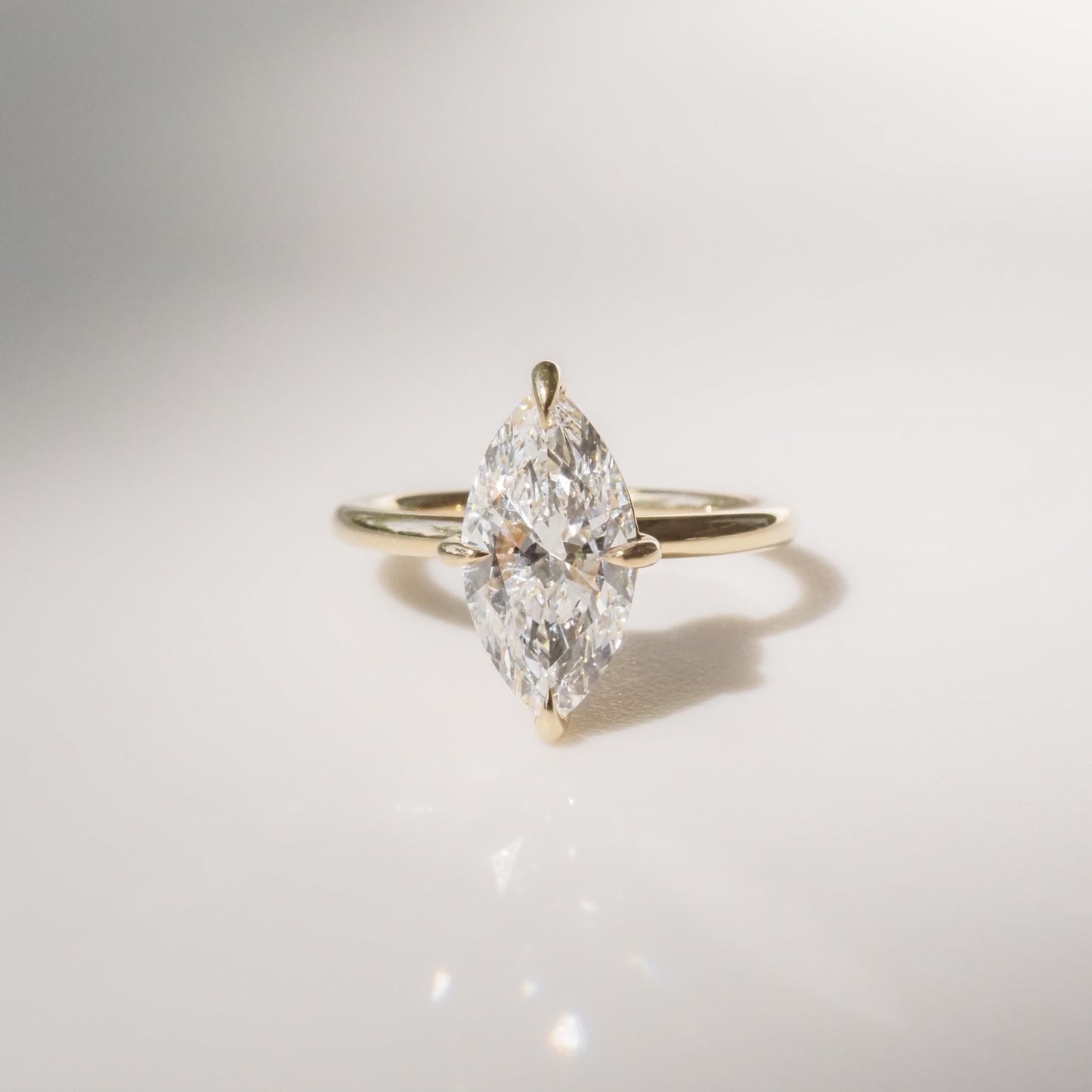 Marquise-cut diamond engagement ring on gold band, elegantly displayed on a smooth white surface, exuding luxury and sophistication.