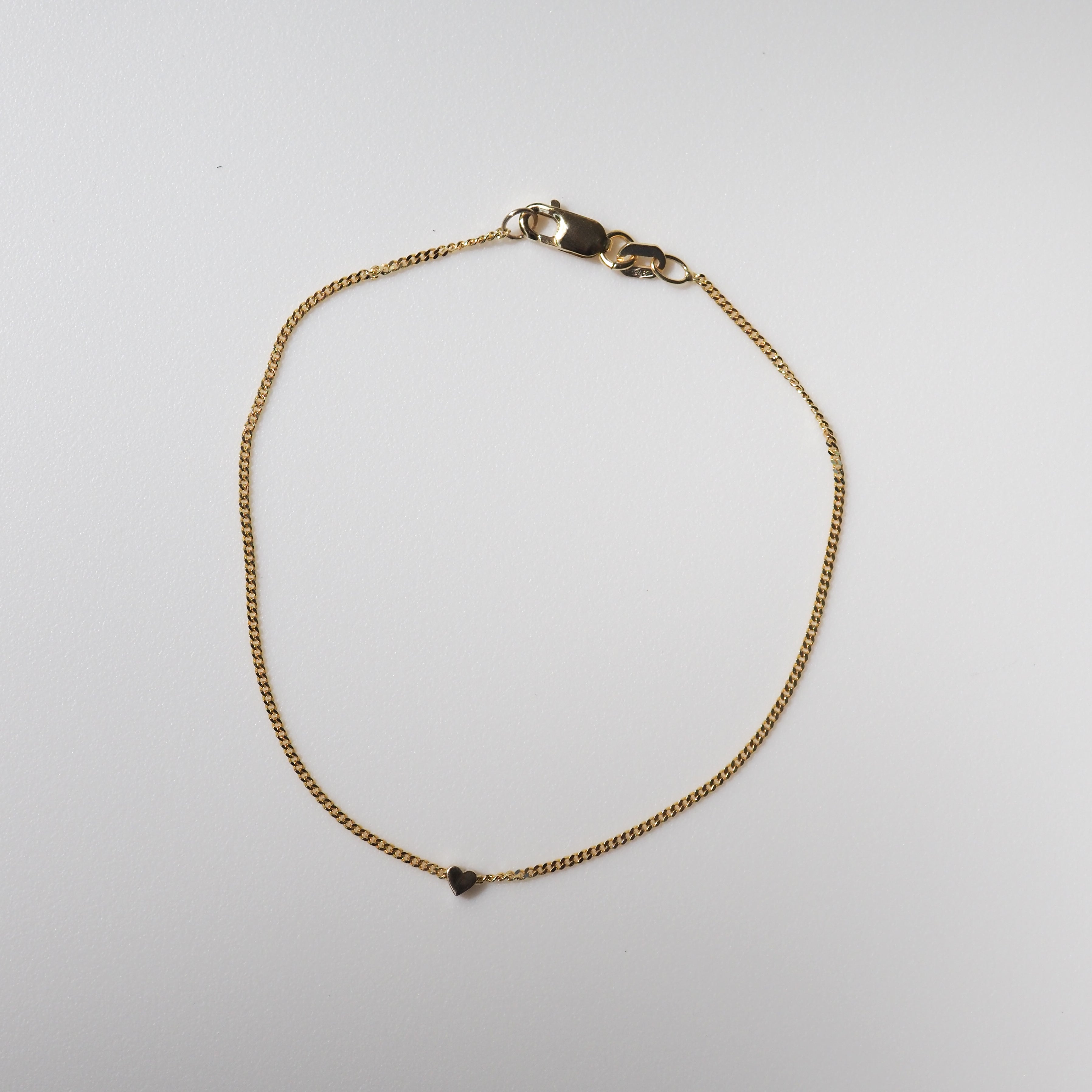 Gold chain bracelet with a heart charm on a white background, showcasing a luxurious and minimalist jewellery design.