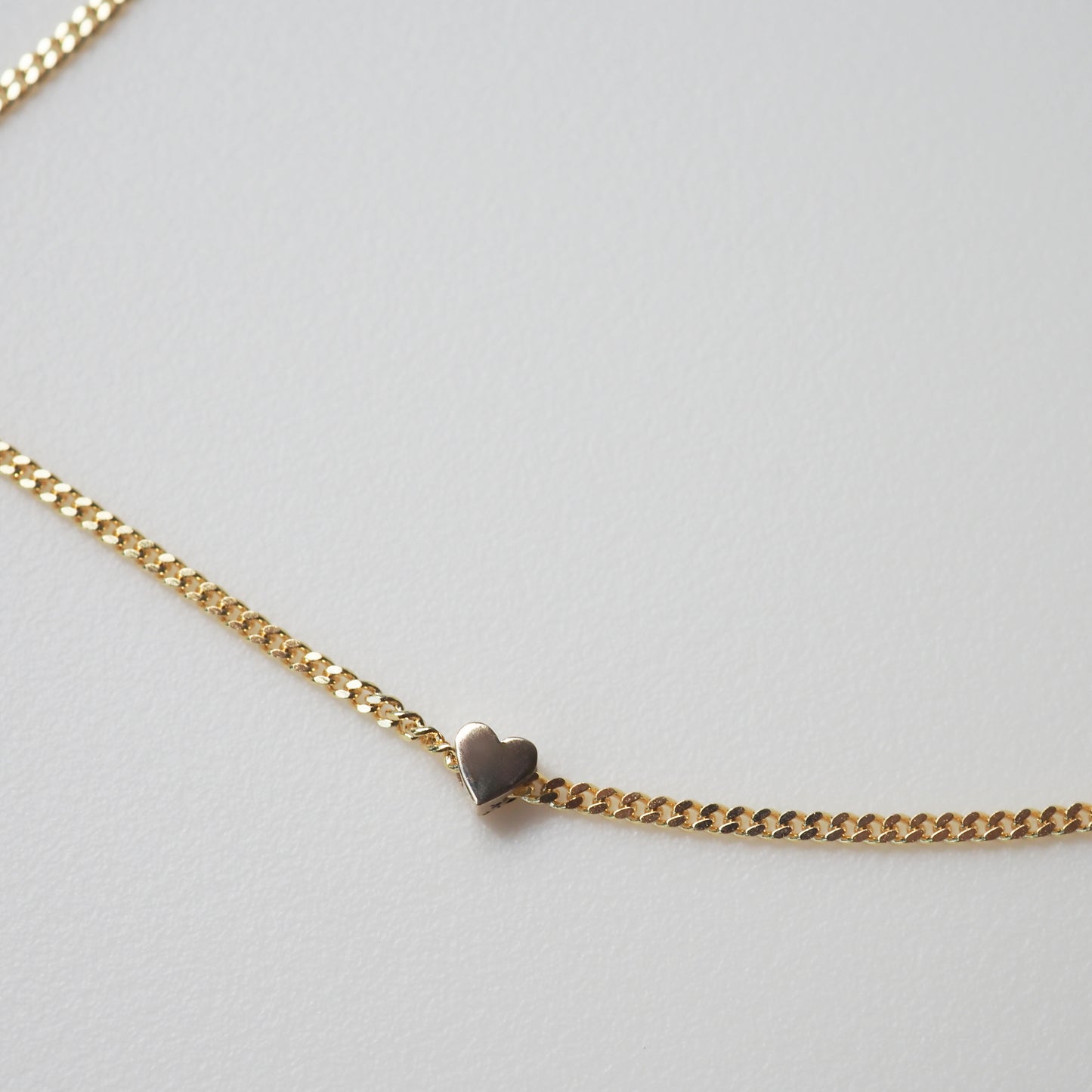 Gold chain necklace with a small heart pendant on a light background. Luxurious, elegant jewellery design.