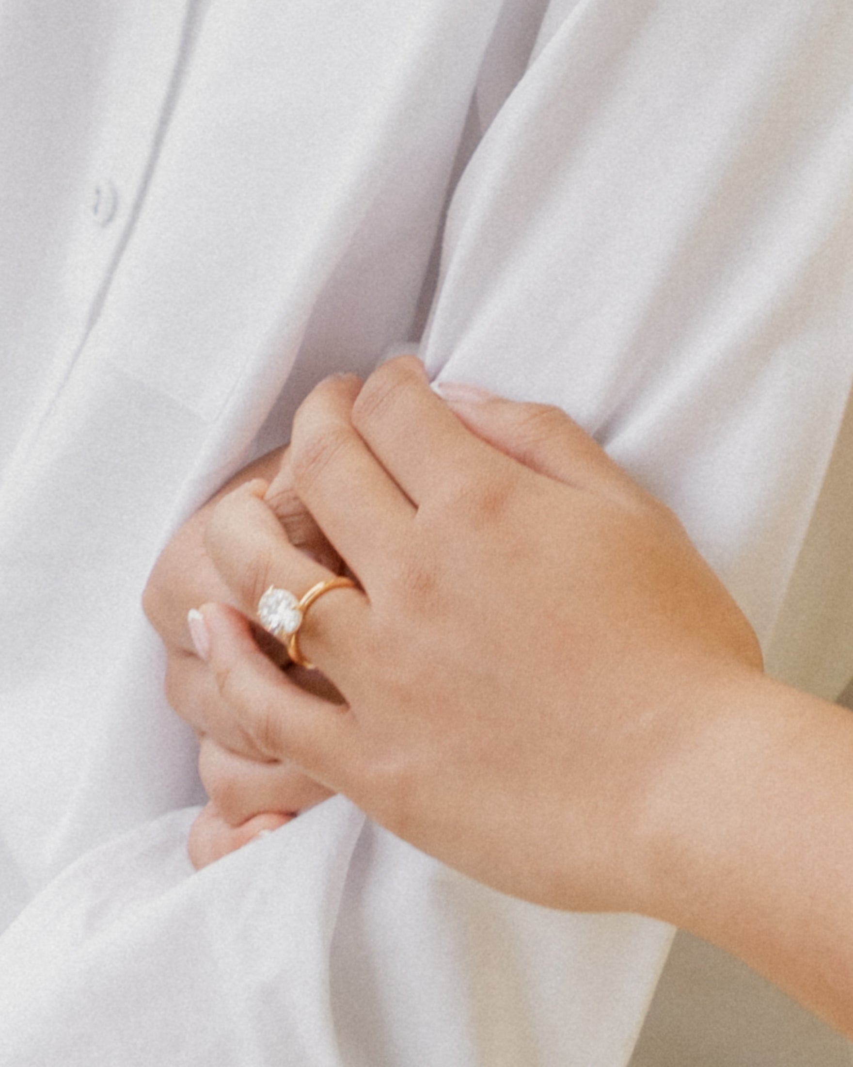 Close-up of a hand with a large diamond ring, gently holding a person in a white shirt, suggesting elegance and luxury jewellery.