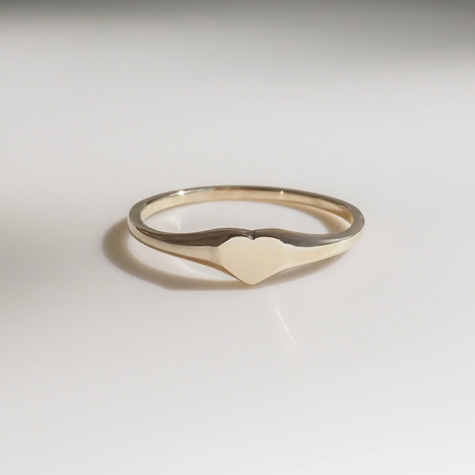 Delicate gold heart ring on a white background, featuring a minimalist design, perfect for luxury jewellery collectors.