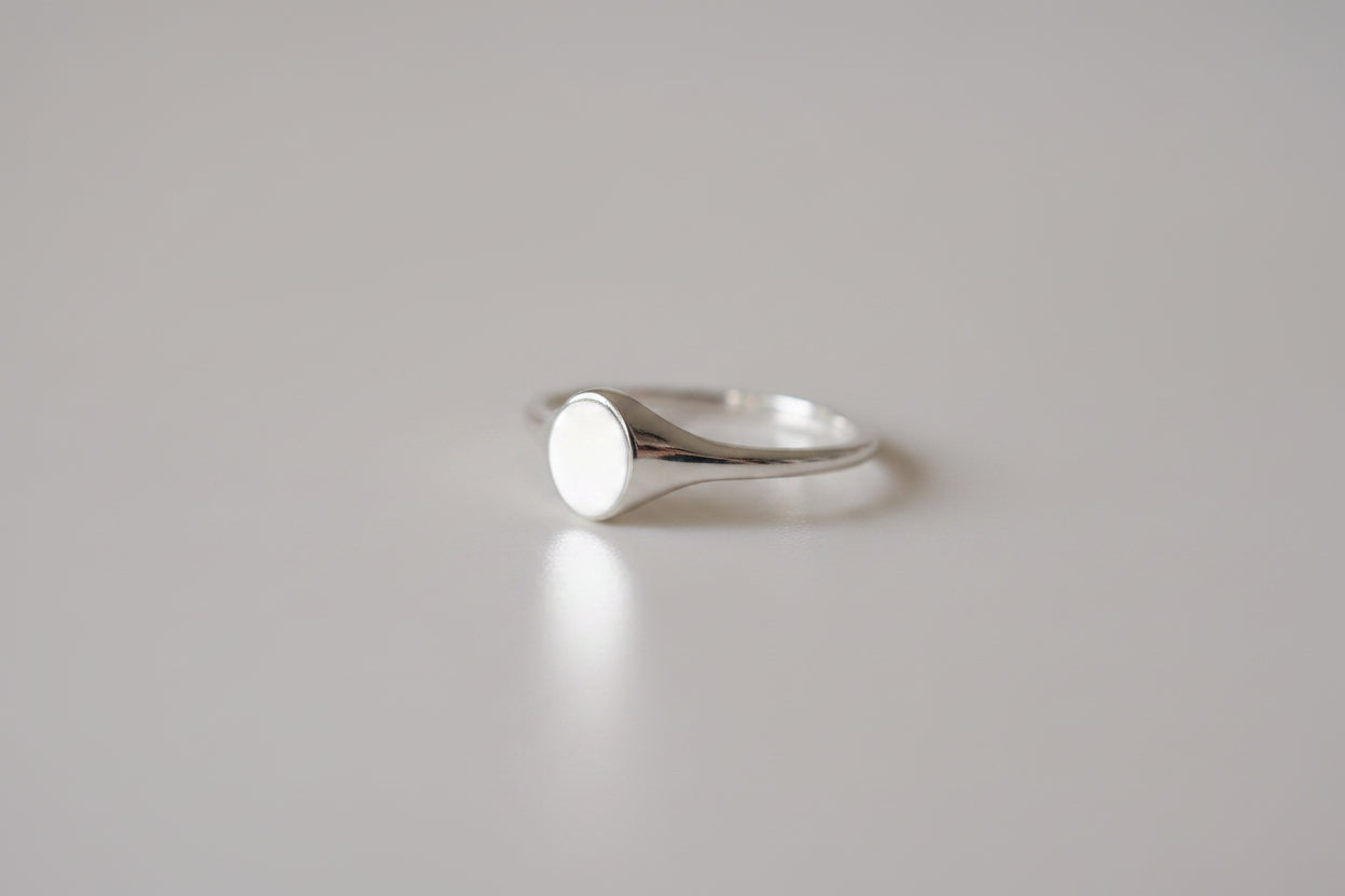 Gold signet ring with a polished oval face on a smooth band, placed on a light grey background. Perfect for luxury jewellery enthusiasts.