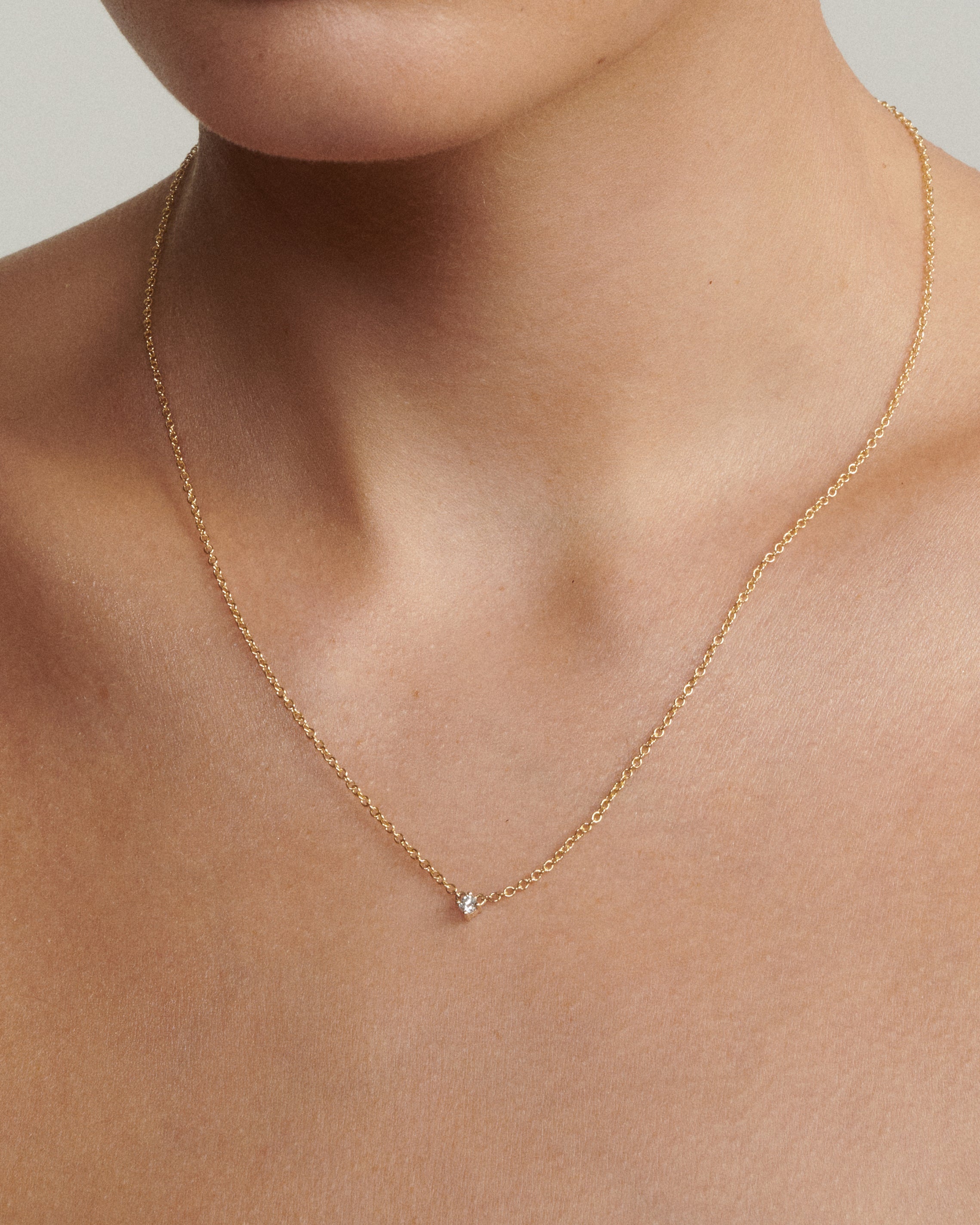 Gold necklace with a small diamond pendant on a woman's neck against a neutral background