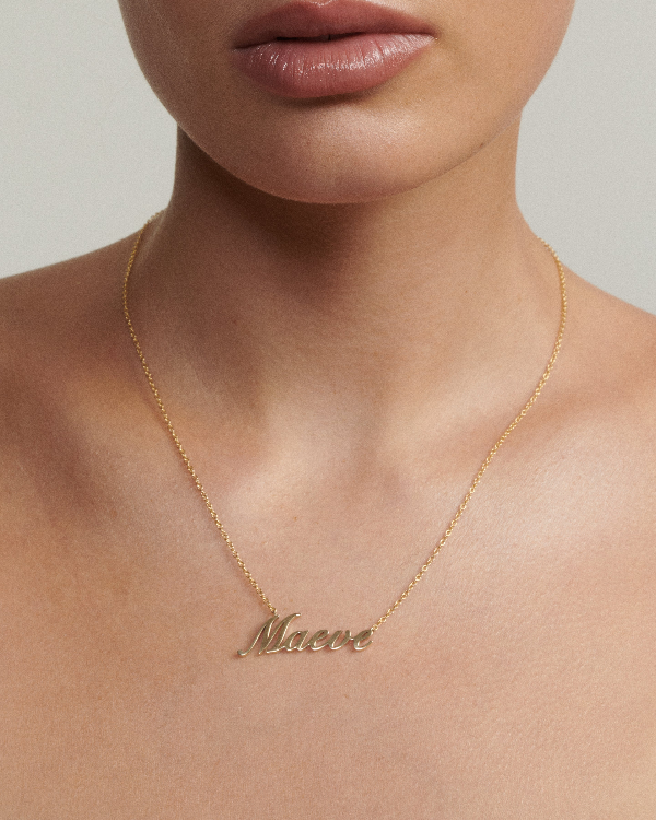 Gold necklace with 'Maeve' pendant on a person's neck against a neutral background