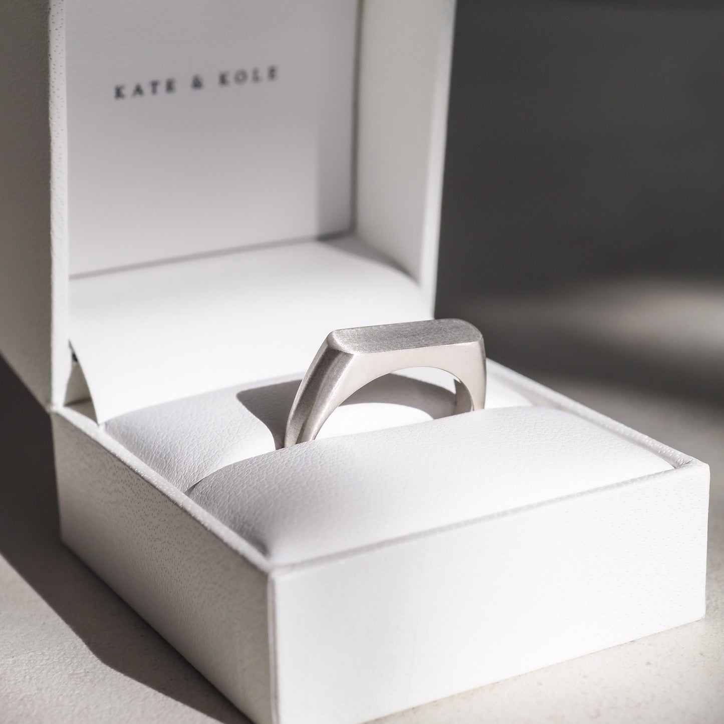 Silver ring in a white Kate & Kole jewellery box, showcasing minimalist luxury design. Light shadows enhance the exquisite premium finish.