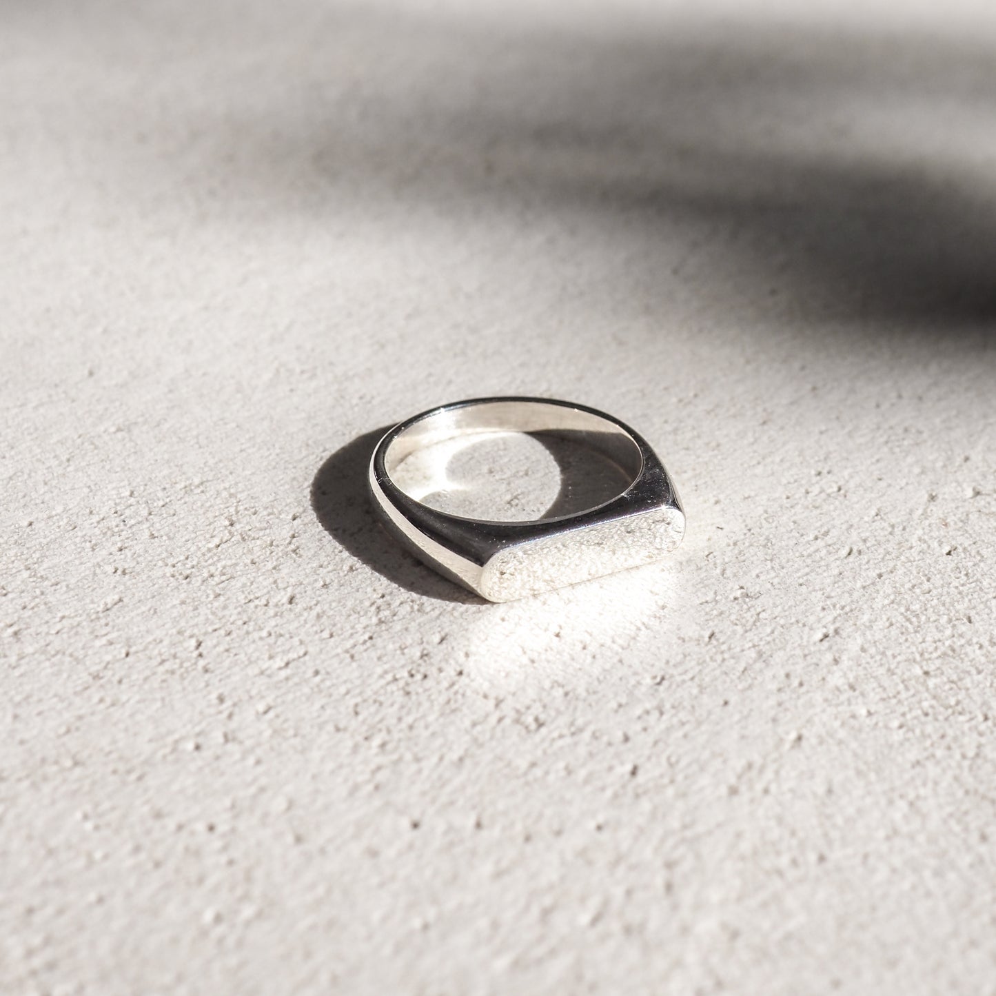 Elegant silver signet ring on textured, light background; soft shadows accentuate its polished finish.