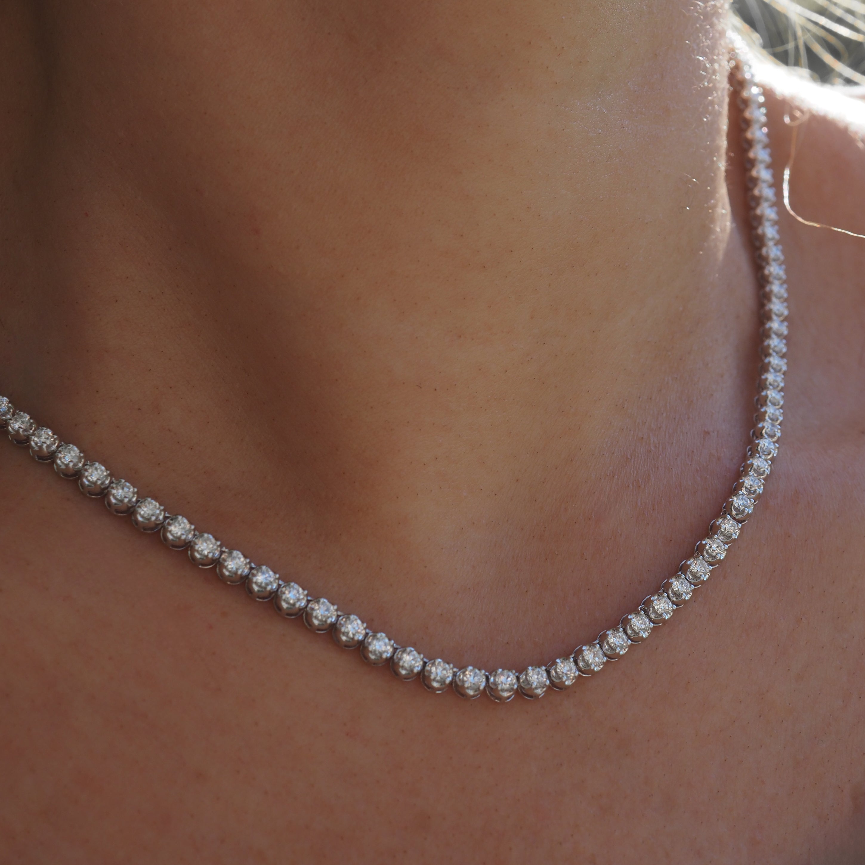 A luxurious diamond tennis necklace elegantly adorns a person's neck, sparkling in soft light, showcasing high-end jewellery craftsmanship.