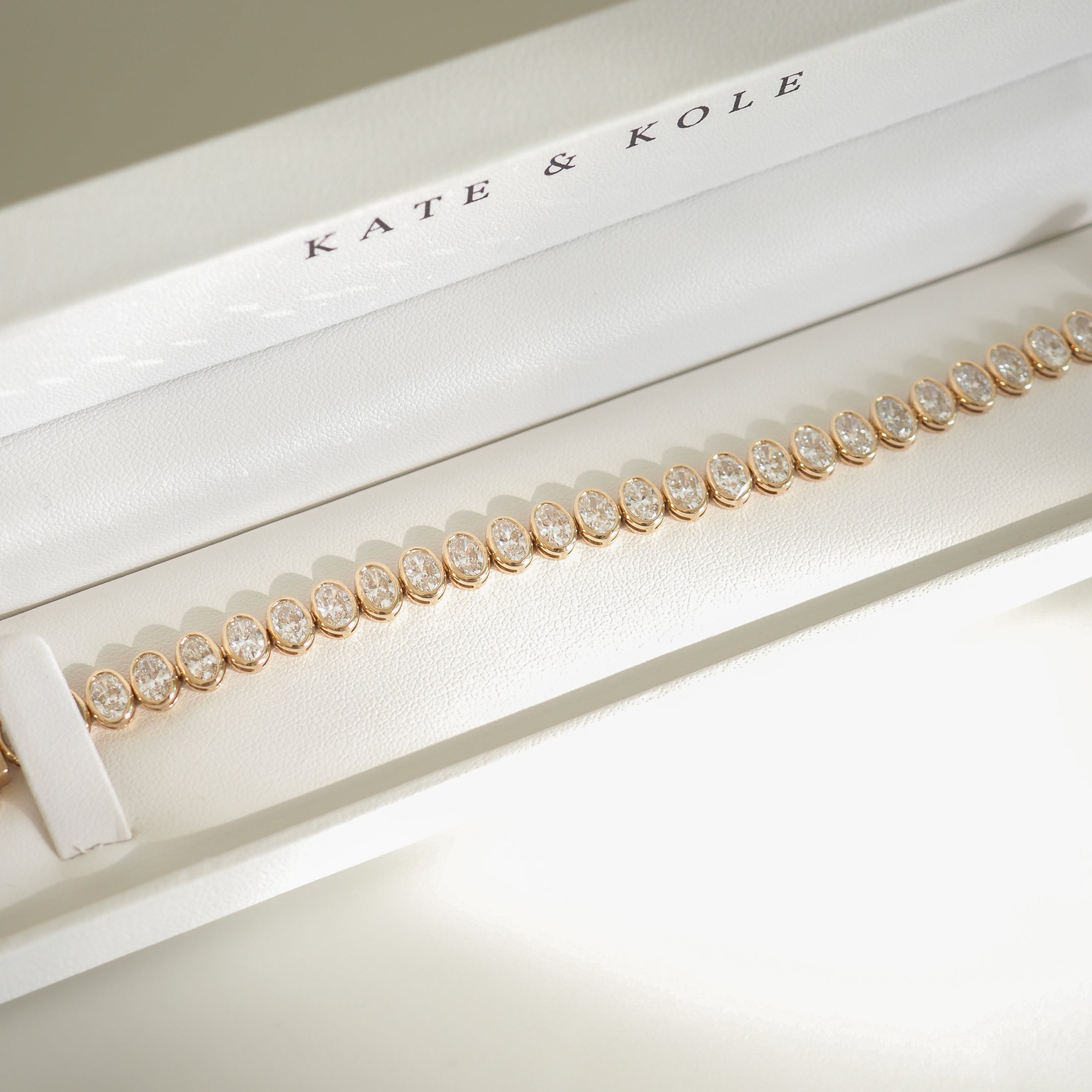 Elegant bracelet in a white box with "KATE & KOLE" branding, featuring gold links and sparkling gemstones. Luxurious jewellery display.