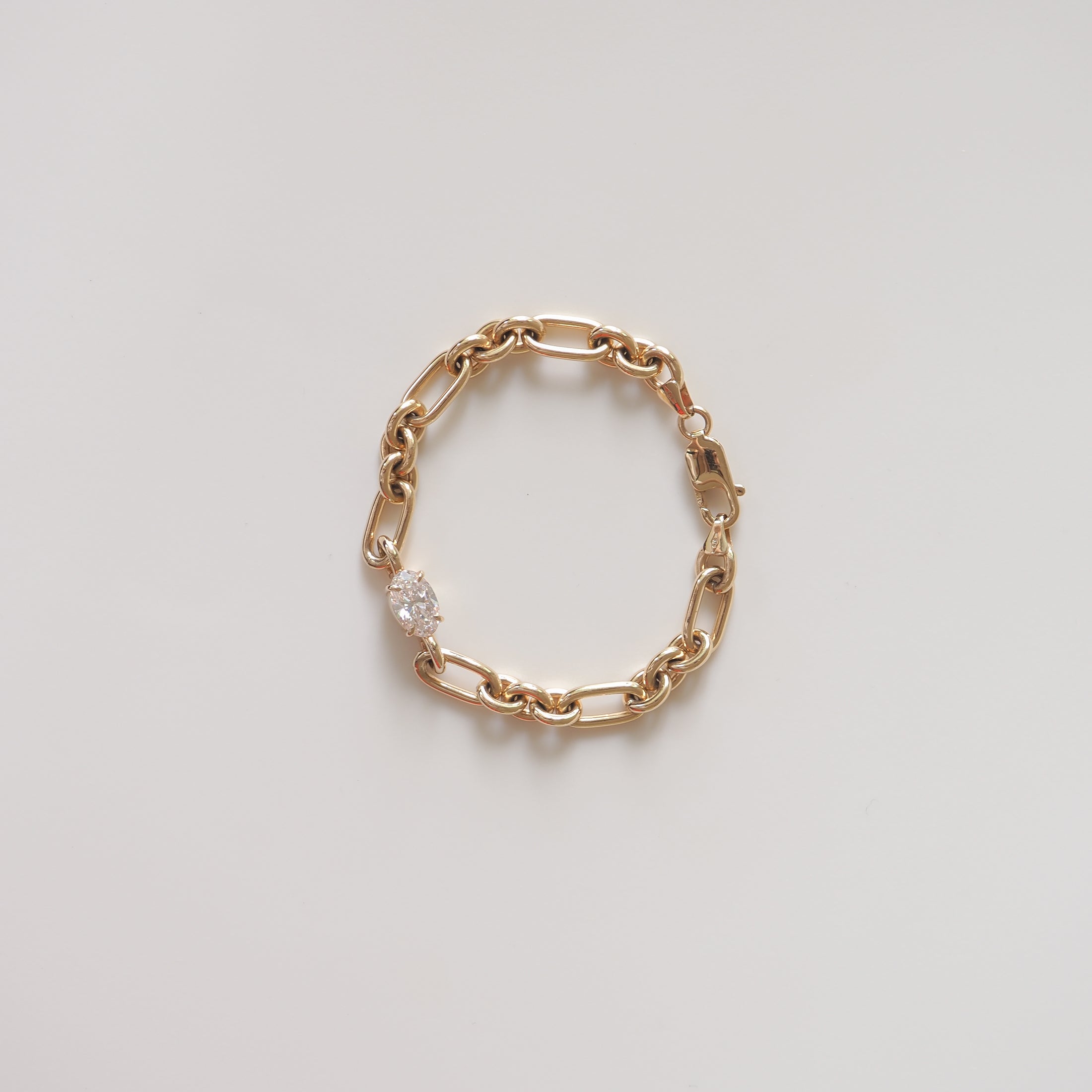 Gold chain bracelet with a cluster of sparkling diamonds on a light grey background. Luxury jewellery, elegant design, high-end style.