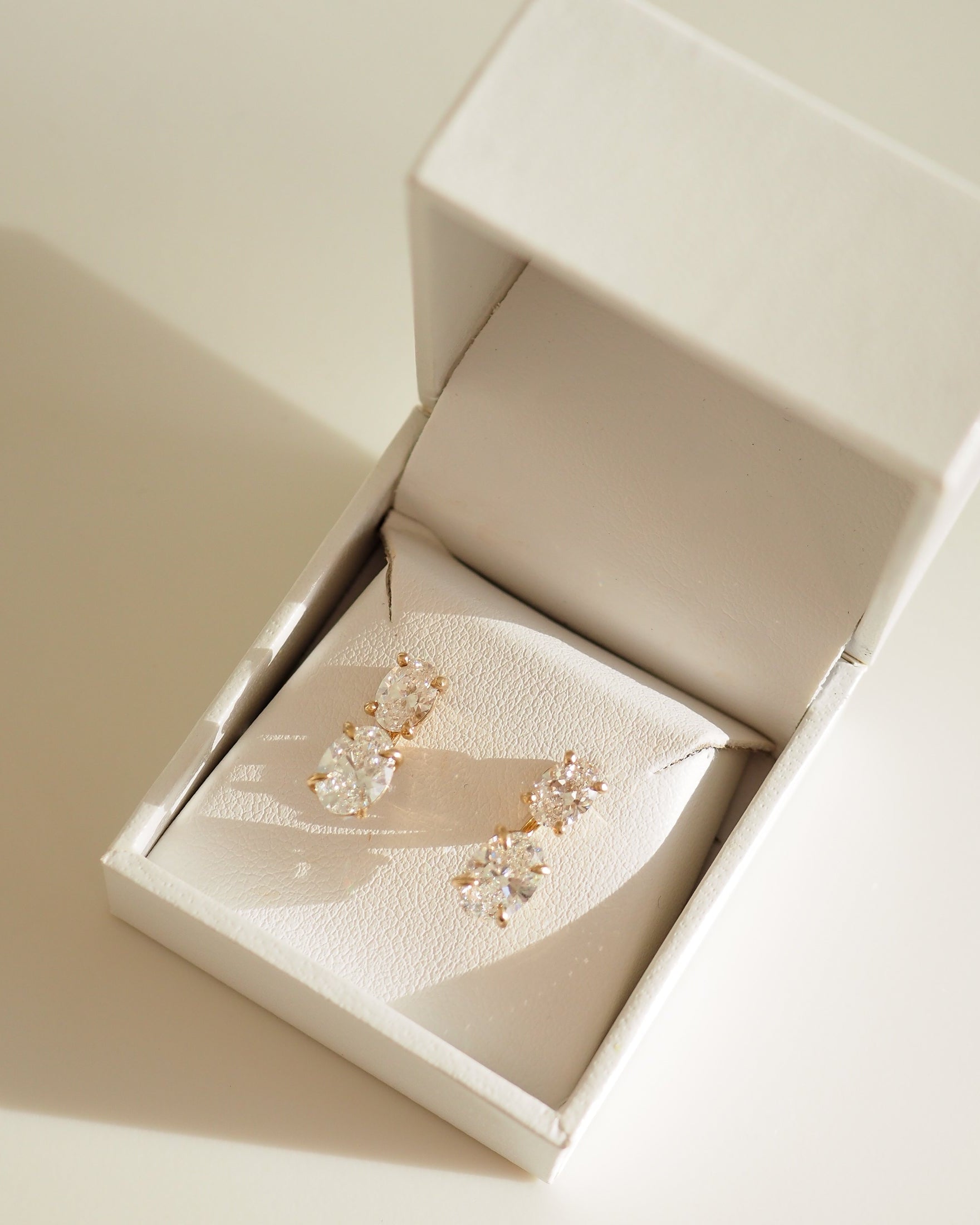 Elegant diamond earrings in a luxurious white jewellery box, illuminated by soft natural light.