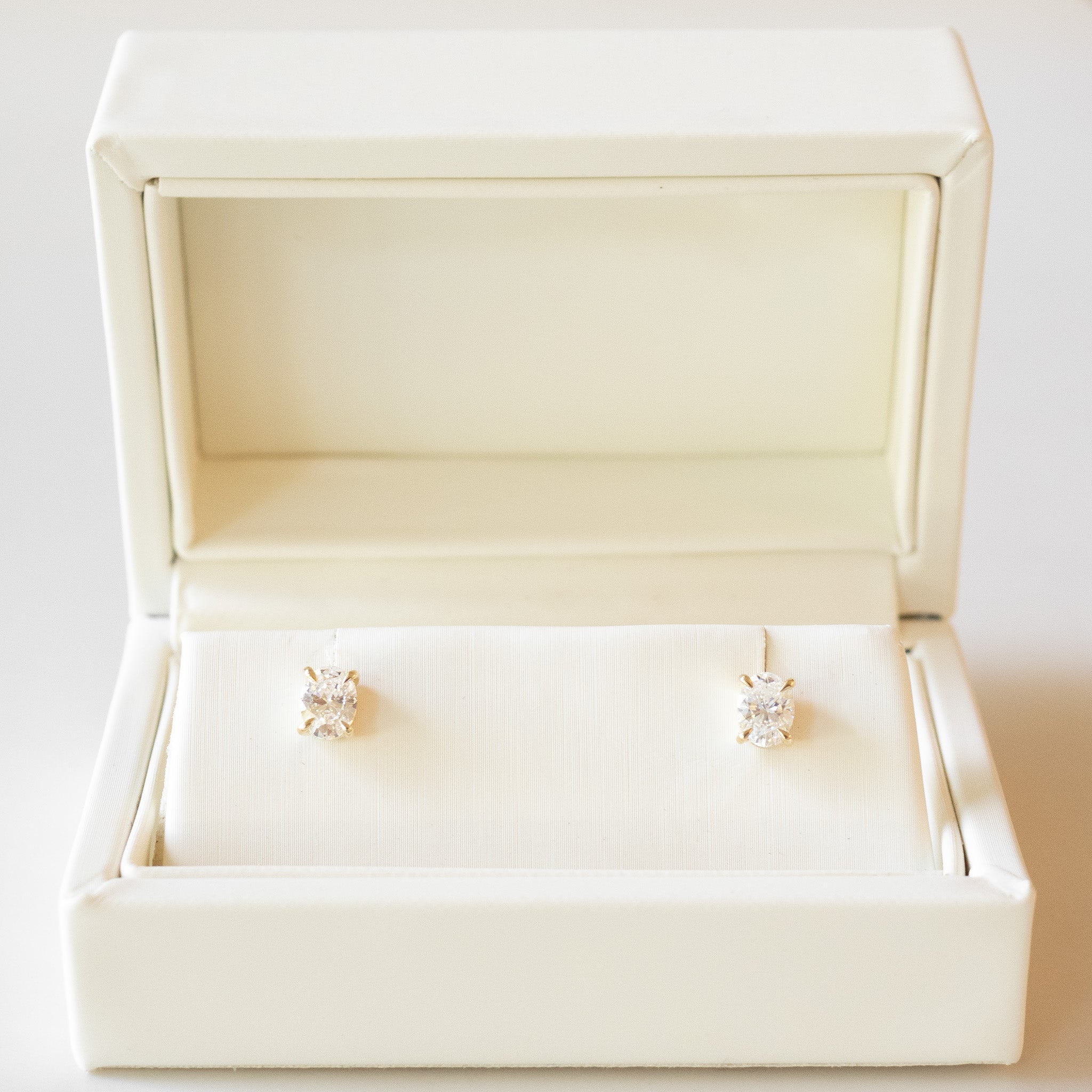 Diamond stud earrings in a white jewelry box on a light background