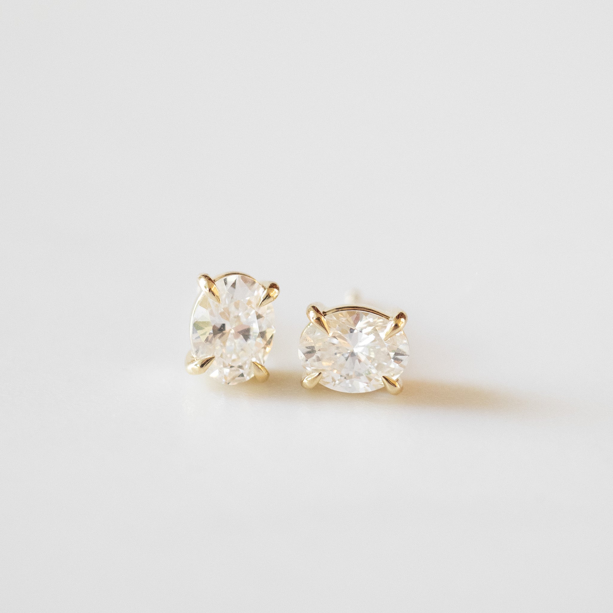 Gold stud earrings with clear gemstones on a light gray background