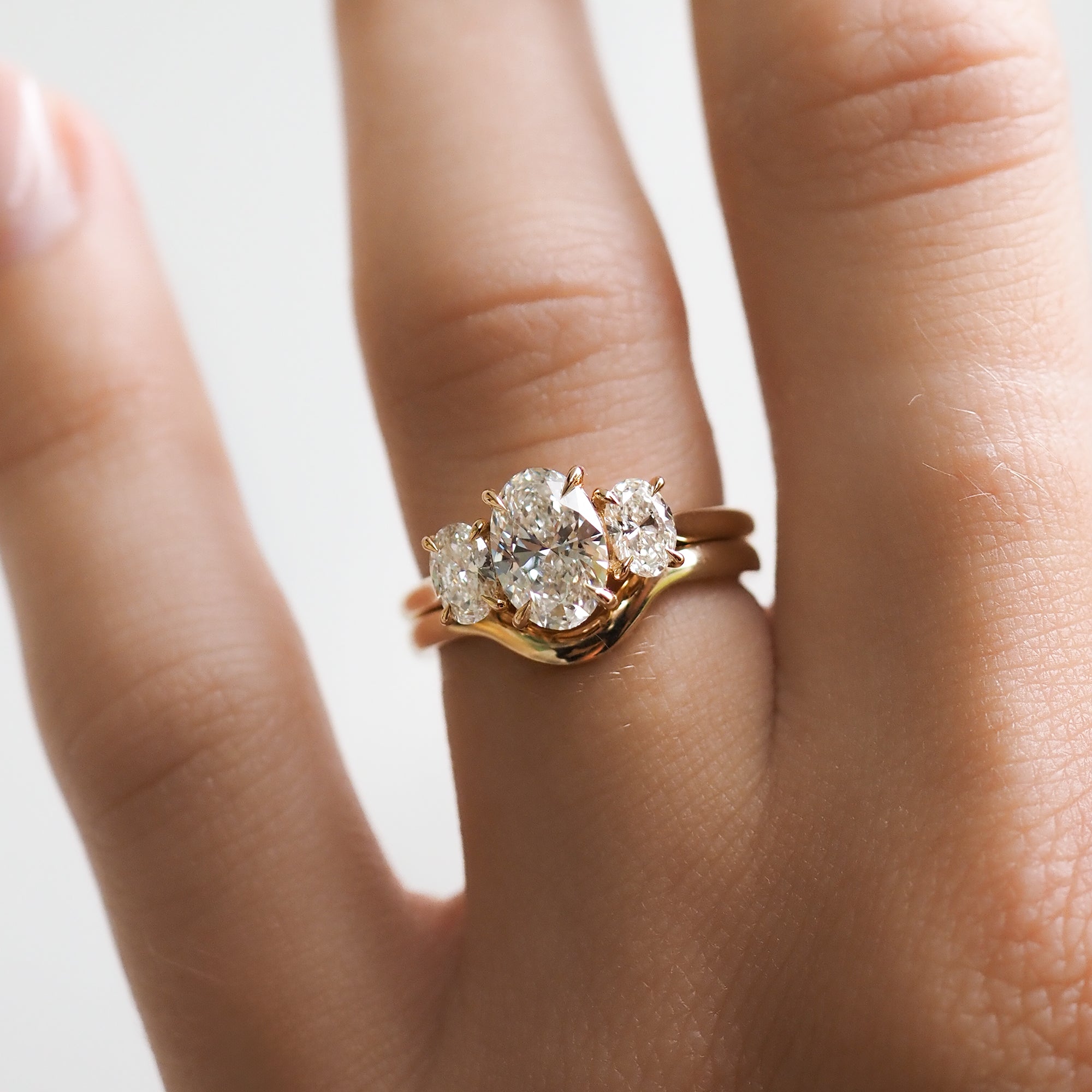 Gold three-stone diamond engagement ring on a hand, featuring sparkling round diamonds. Luxury, high-end jewellery design.
