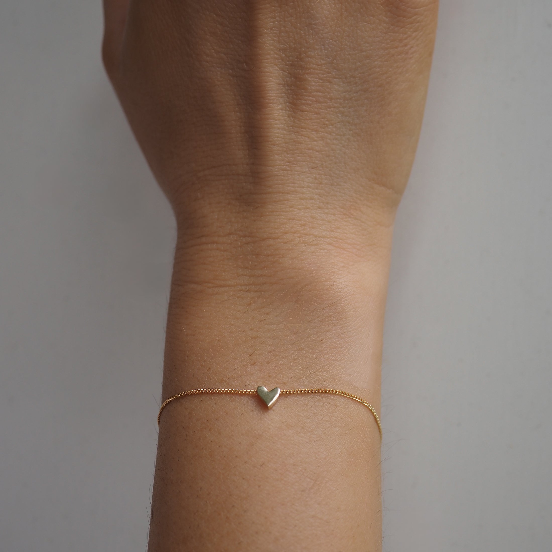 Gold bracelet with a delicate heart charm on a person's wrist. Minimalistic luxury jewellery.