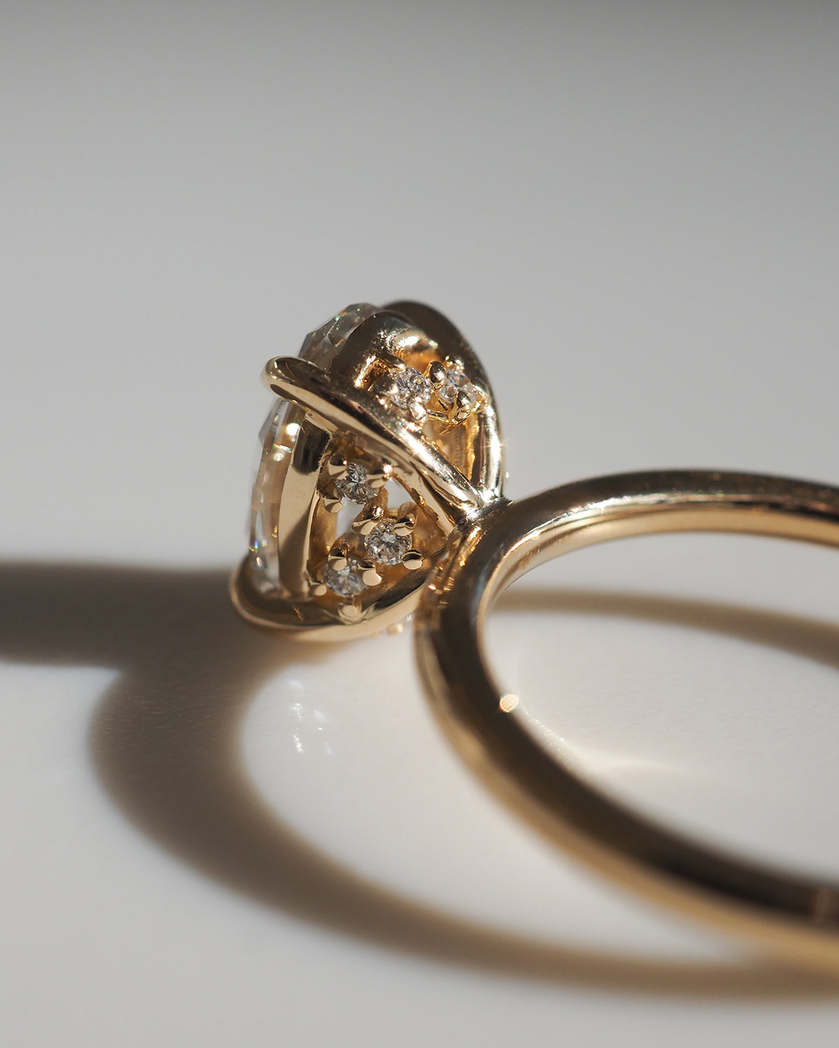 Close-up of a gold ring with a cluster of sparkling diamonds, casting a soft shadow on a white surface. Luxurious jewellery design.