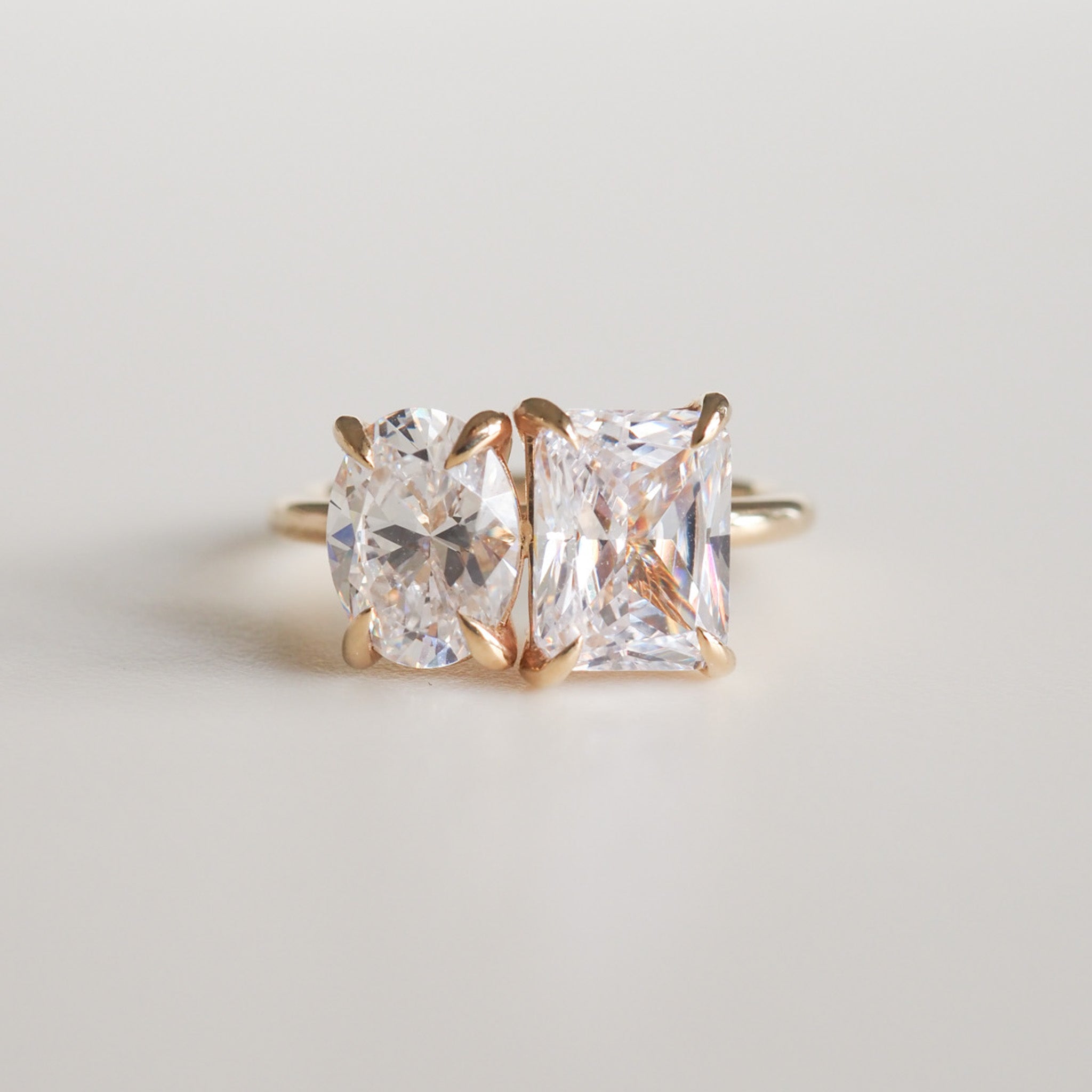 Elegant ring with two adjacent diamonds, oval and rectangular, set in gold. Luxurious jewellery piece on a neutral background.