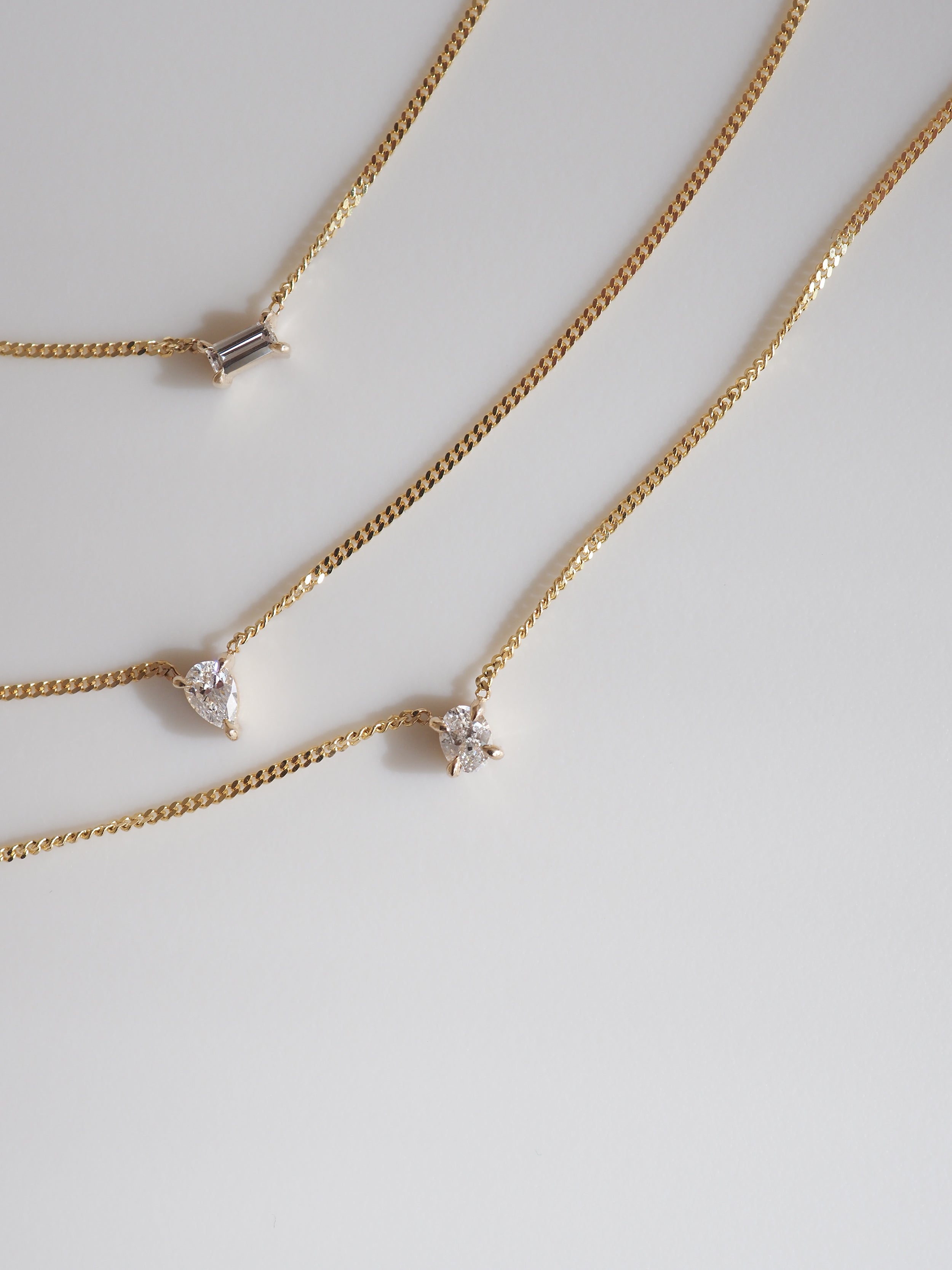 Three gold necklaces with elegant diamond pendants, featuring a baguette, heart, and star shape, displayed on a light background.