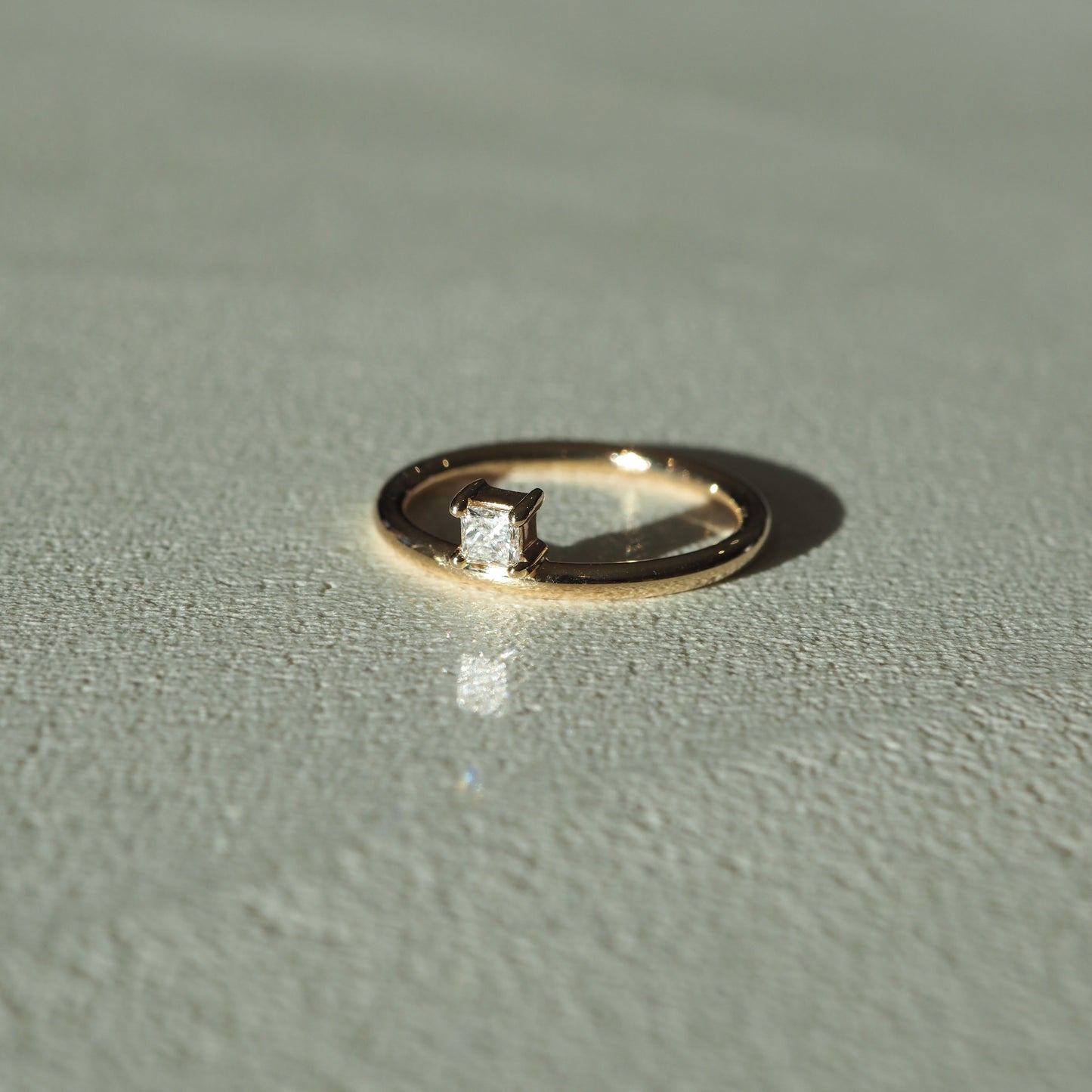 Gold ring with a square-cut diamond on textured surface, lit by soft light. Luxurious jewellery piece, elegant and minimalist in design.