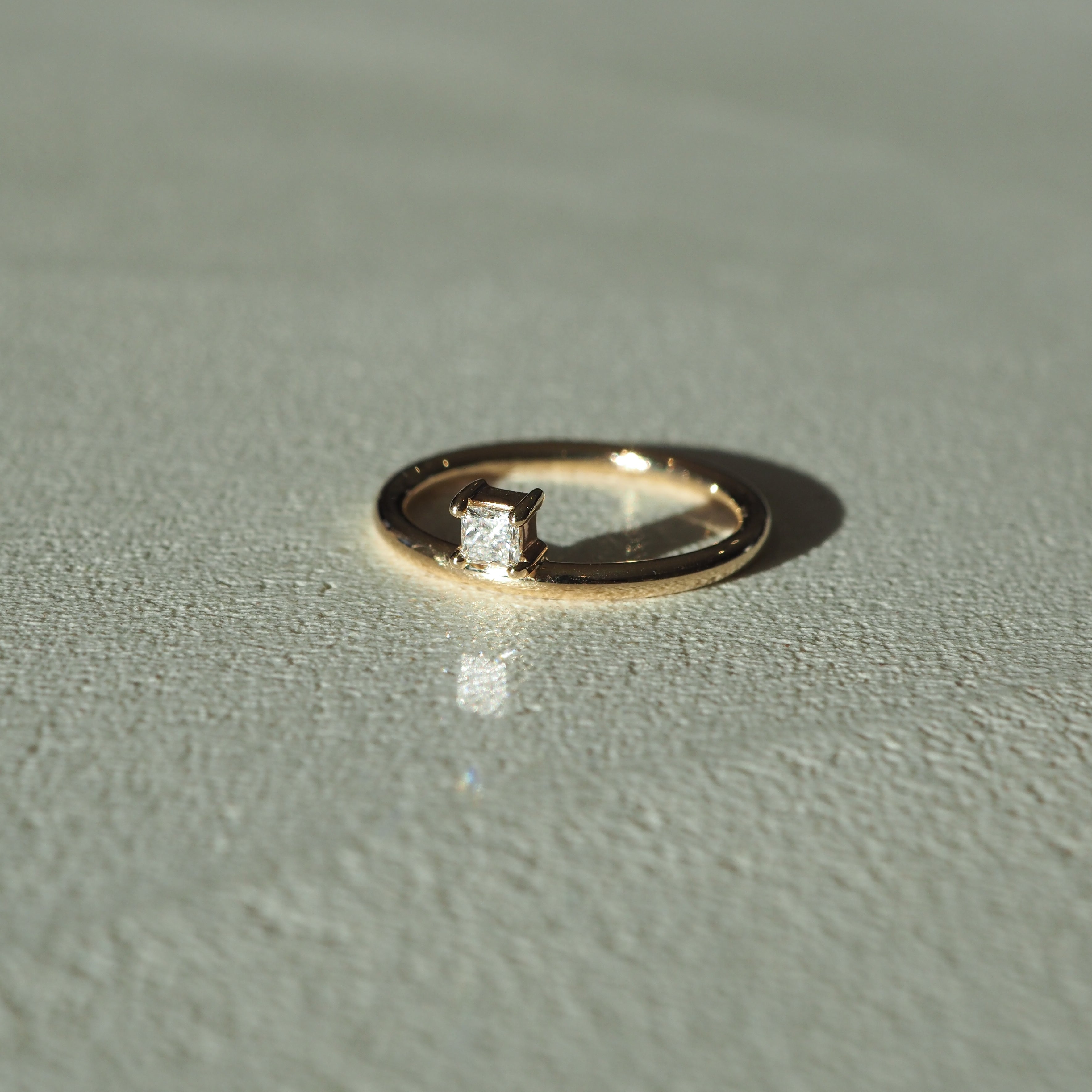 Gold ring with a square-cut diamond on textured surface, lit by soft light. Luxurious jewellery piece, elegant and minimalist in design.