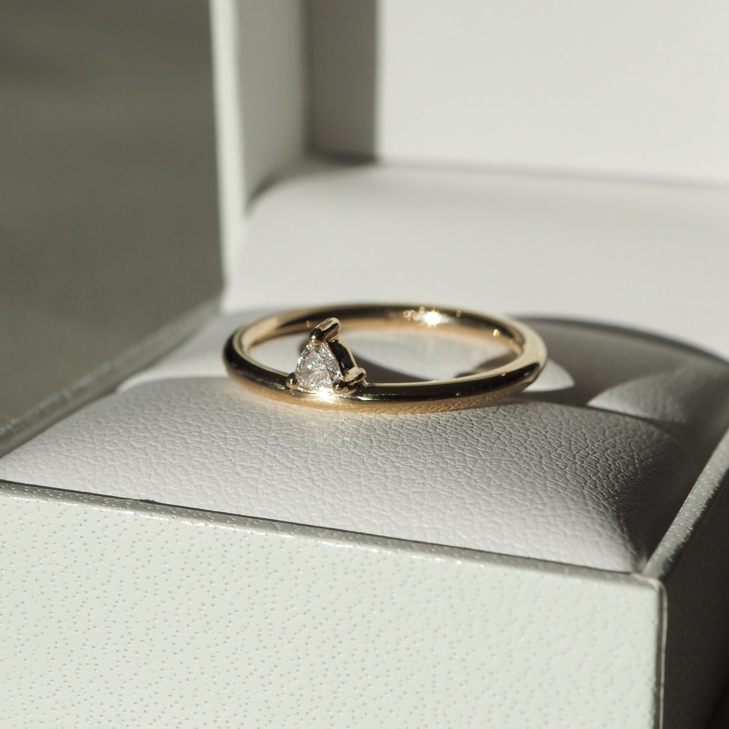 Gold ring with a solitaire diamond on a white leather jewellery box, lit by natural sunlight, showcasing luxury and elegance.