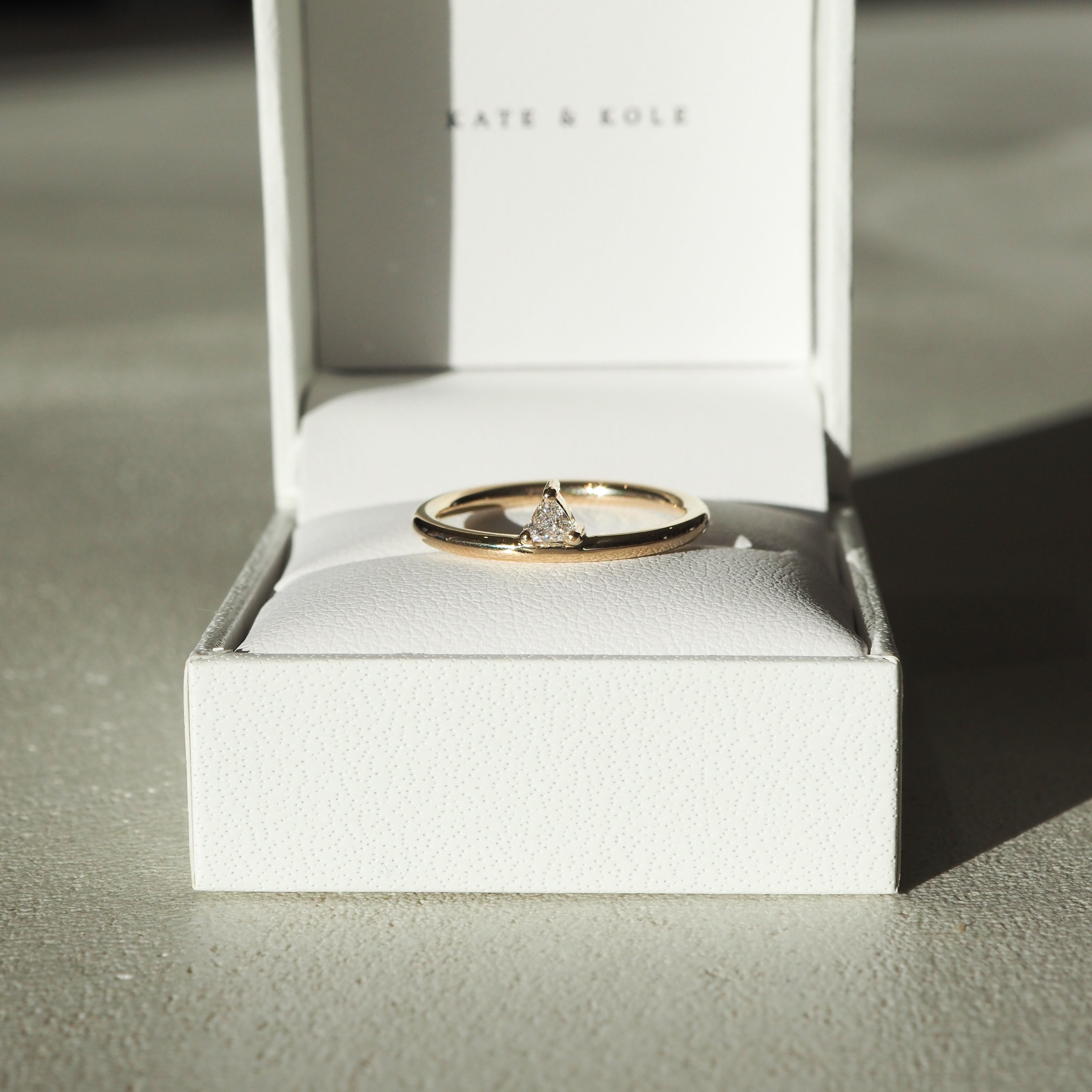 Gold triangle-cut diamond ring in a white Kate & Kole jewellery box, bathed in soft light, perfect for luxury fashion and jewellery lovers.