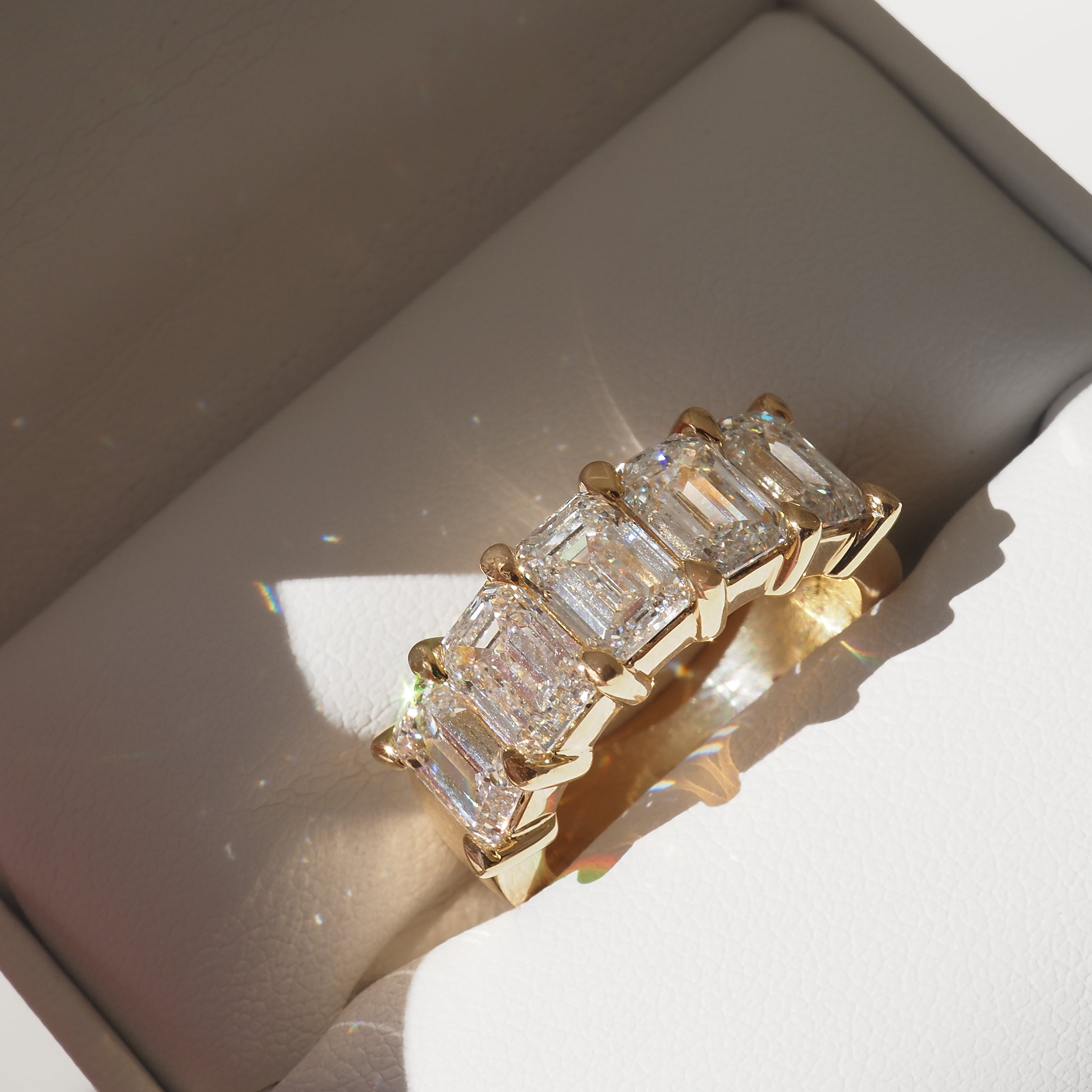 Gold ring with five rectangular-cut diamonds in a sunlit jewellery box. Luxurious design showcasing high-end craftsmanship and elegance.