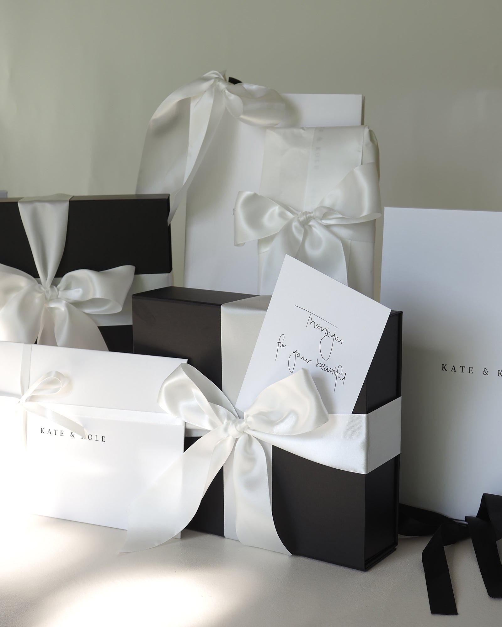 Luxurious black and white gift boxes with elegant white ribbons, featuring a handwritten 'Thank you' card. Stylish jewellery packaging.