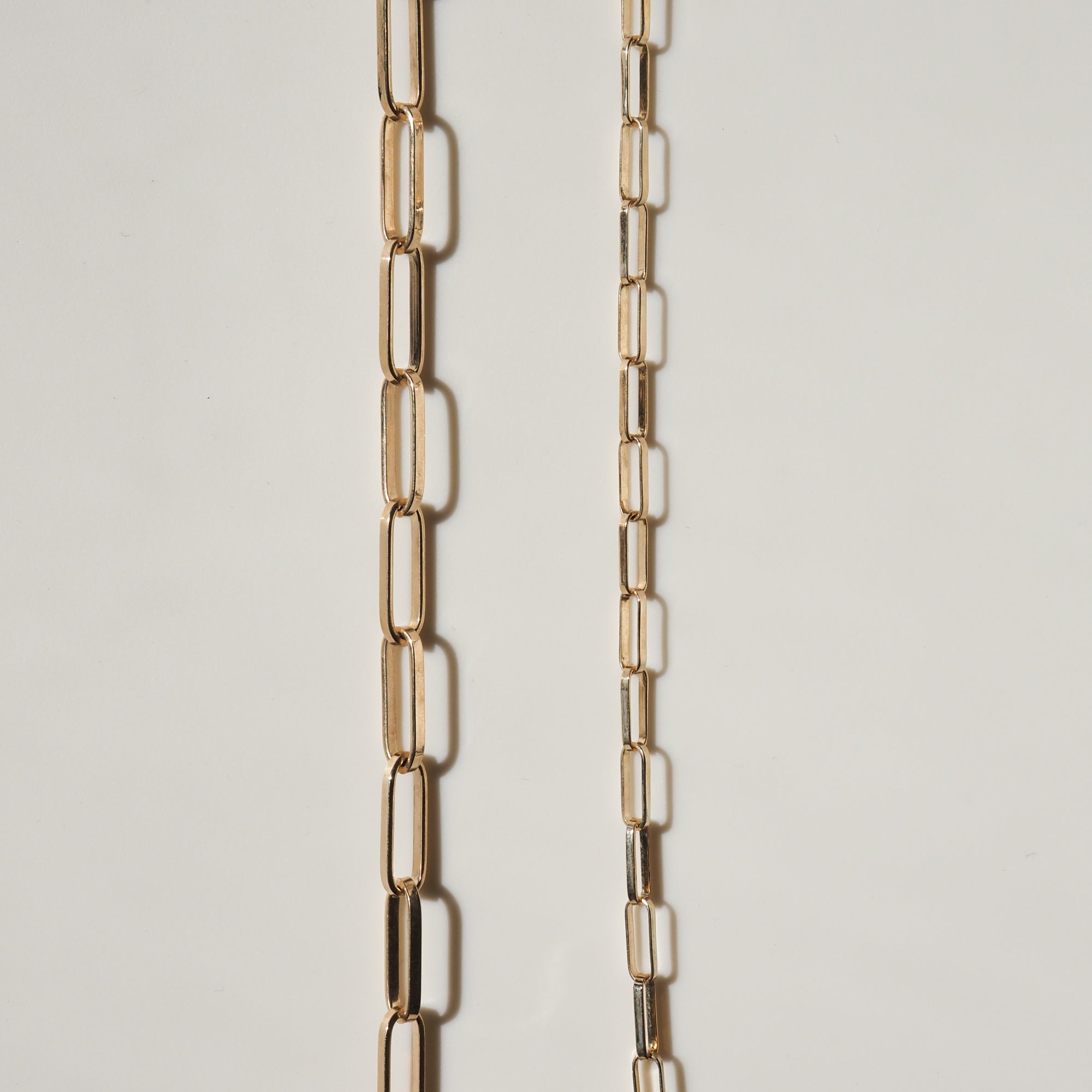 Two elegant gold chain necklaces with elongated rectangular links on a light background, showcasing luxury and high-end jewellery design.