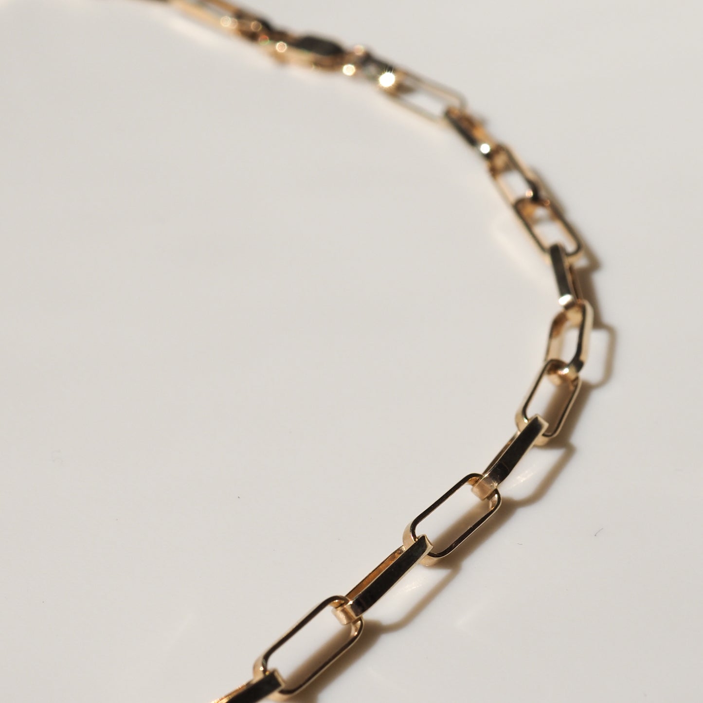 Close-up of a delicate gold chain necklace with rectangular links on a white background, showcasing luxury jewellery craftsmanship.
