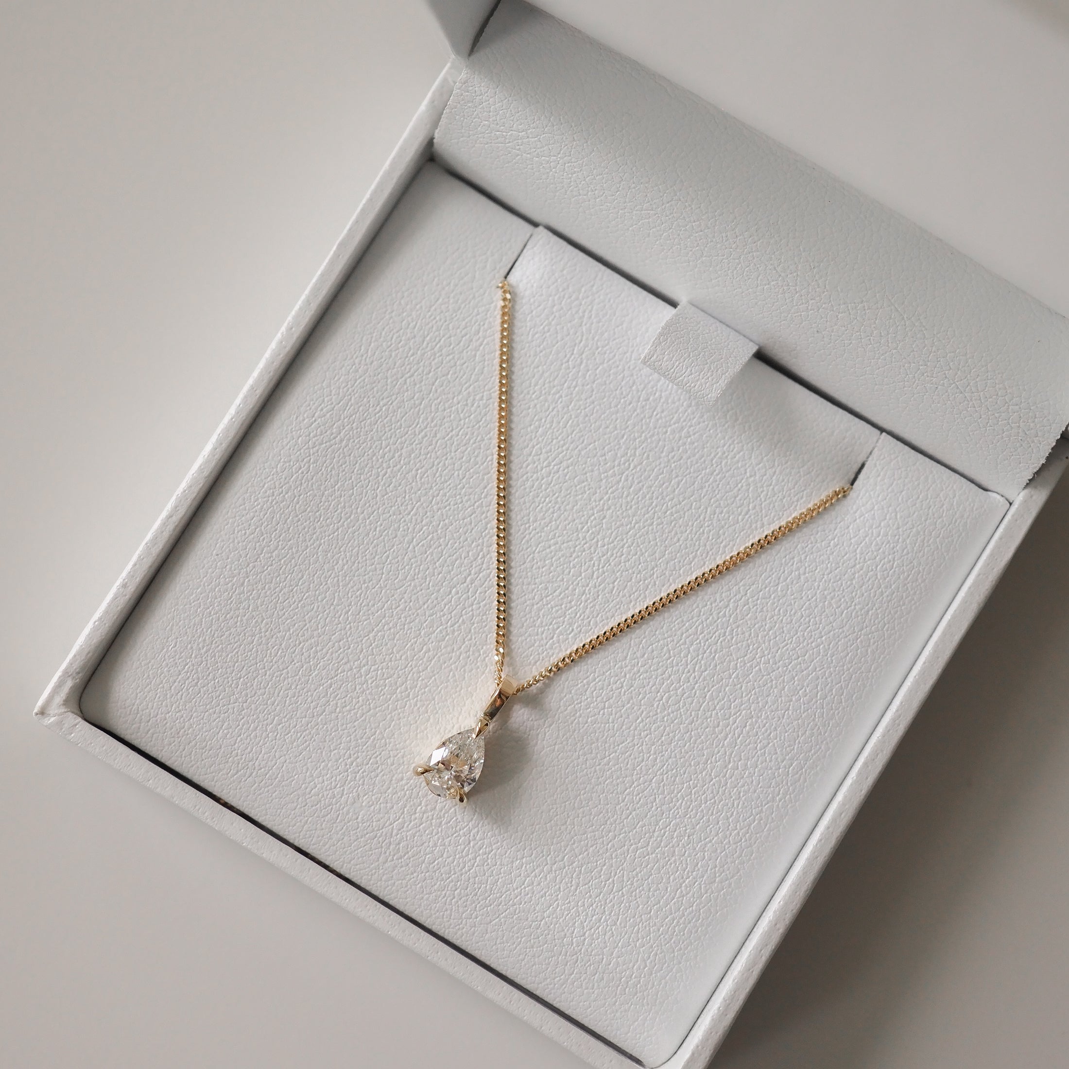 Gold chain necklace with a teardrop diamond pendant in an open white jewellery box. Luxurious, elegant design.