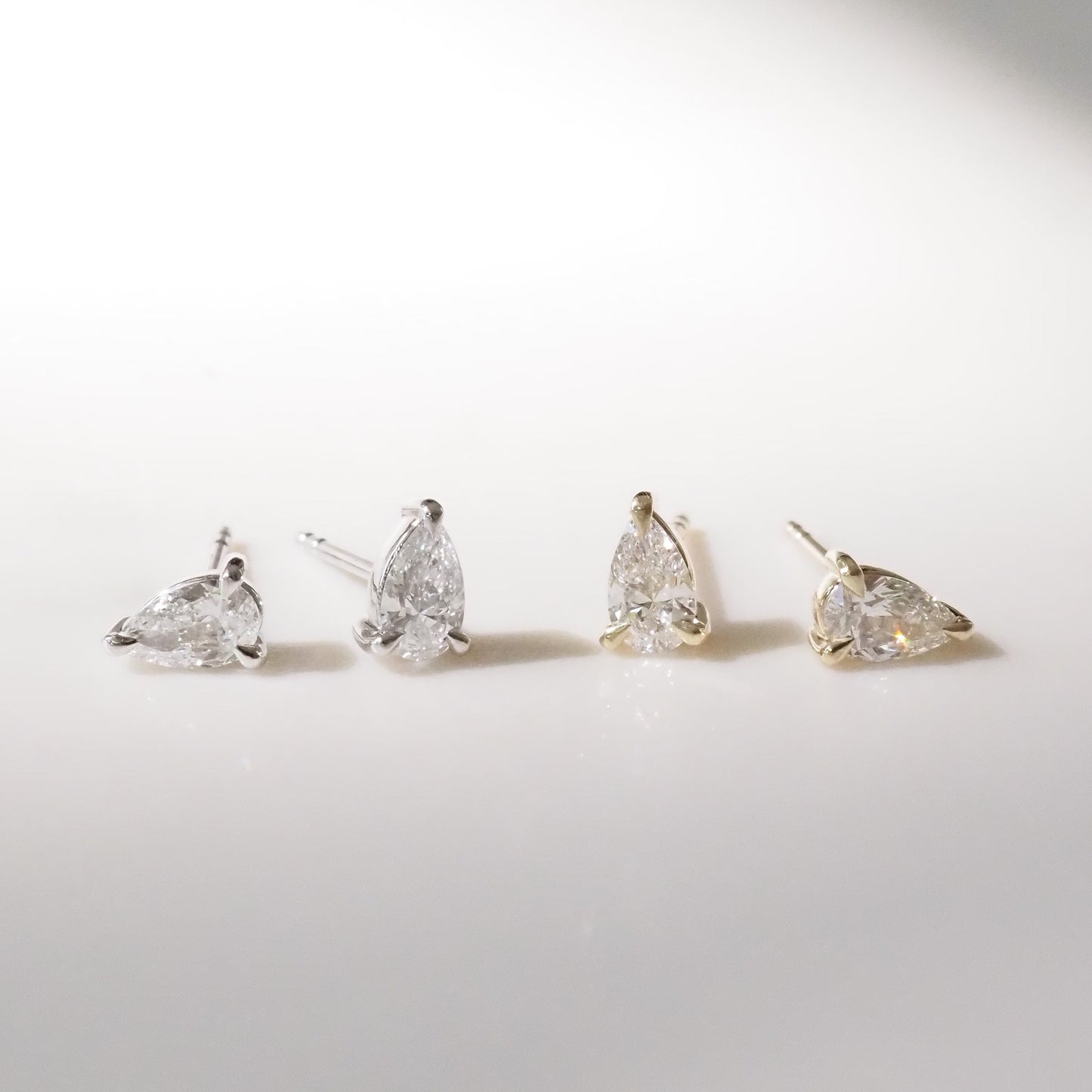 Four pear-shaped diamond earrings on a light gray background