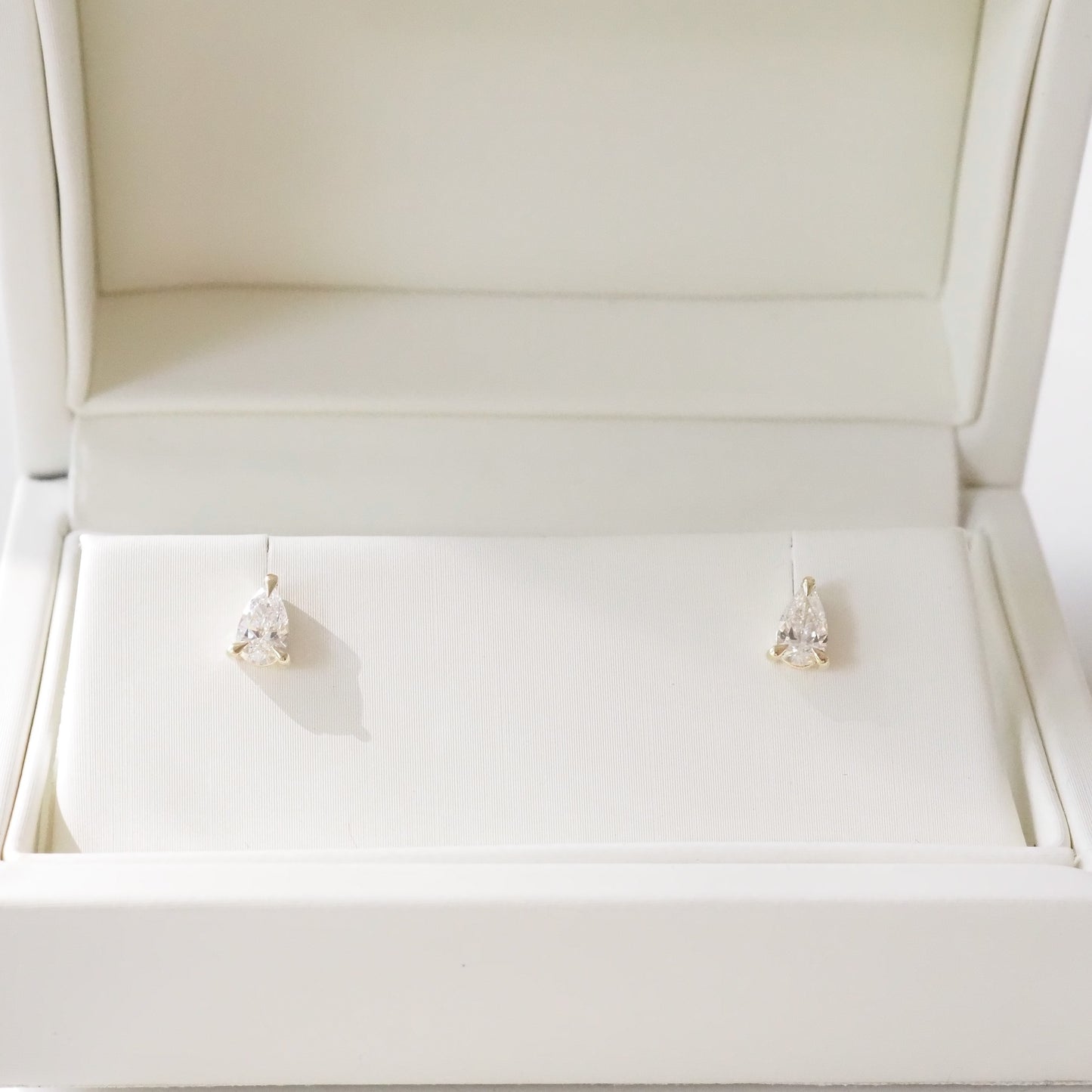 Open beige jewelry box with pear diamond earrings inside on a white background