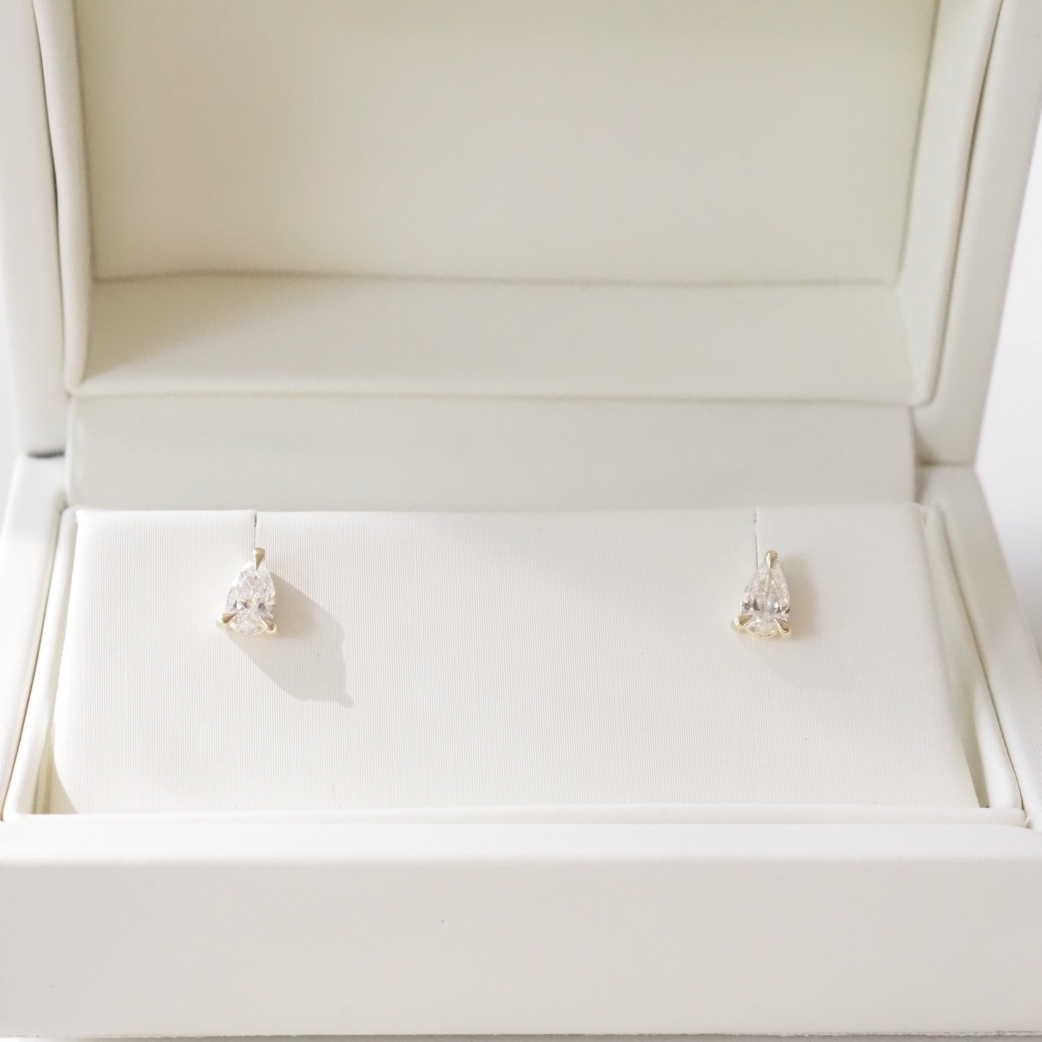 Open beige jewelry box with pear diamond earrings inside on a white background