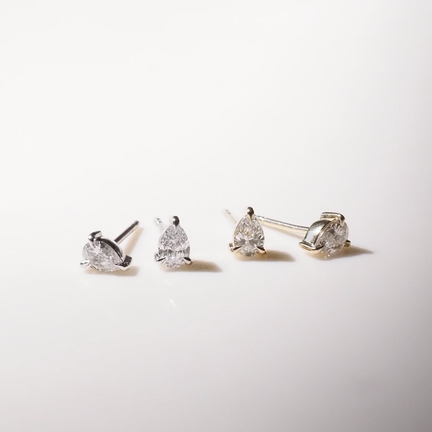Four pear diamond stud earrings on a light gray background