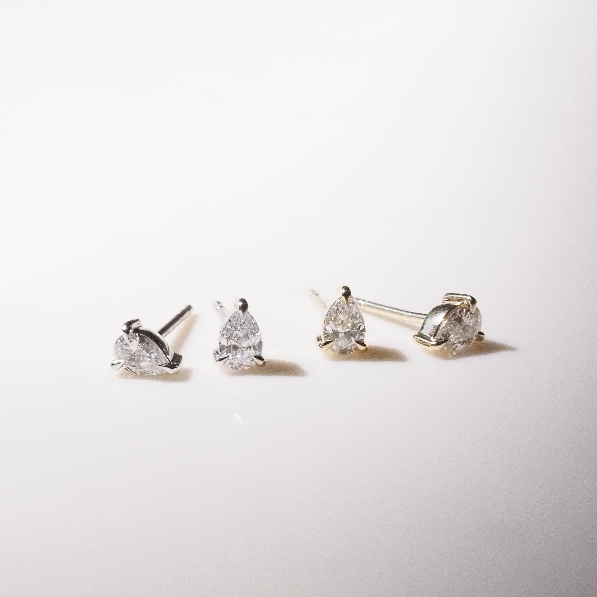 Four pear diamond stud earrings on a light gray background