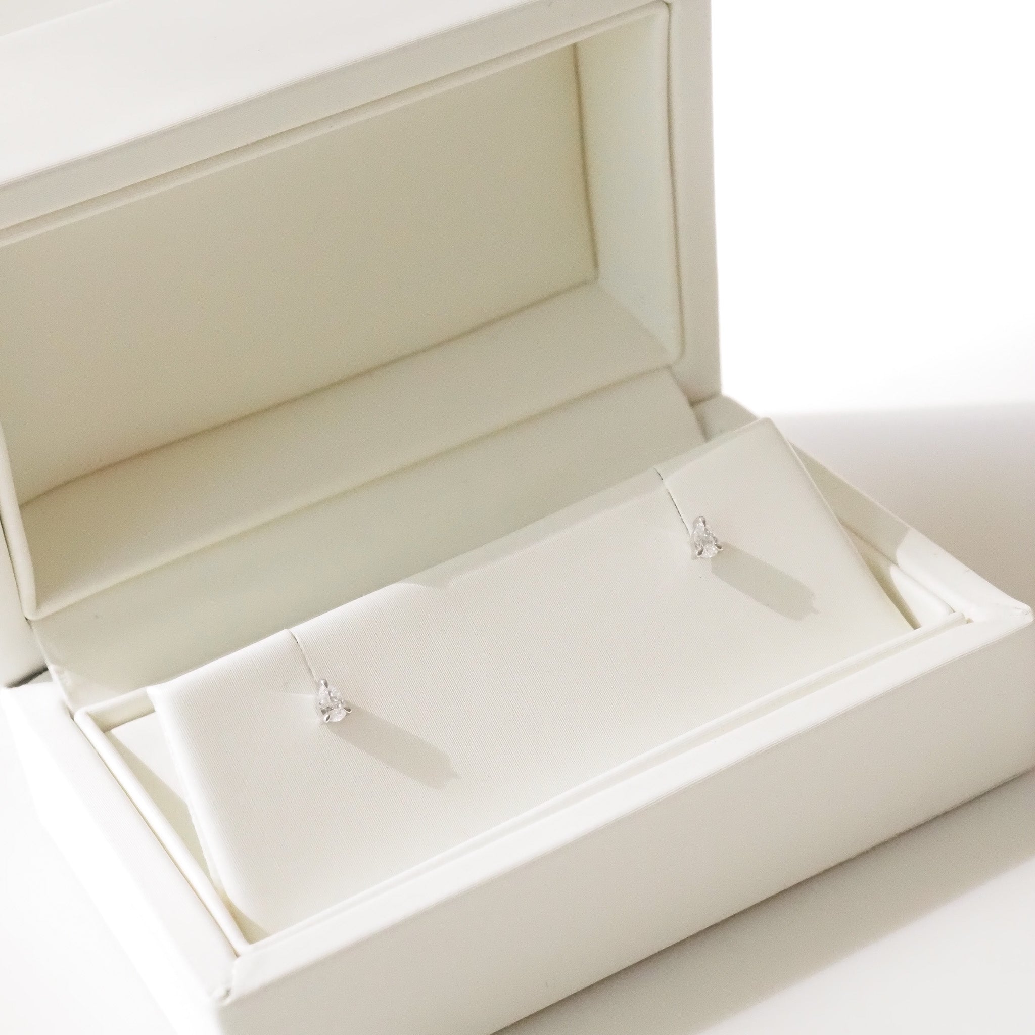 Open beige jewelry box with pear earrings inside on a white background
