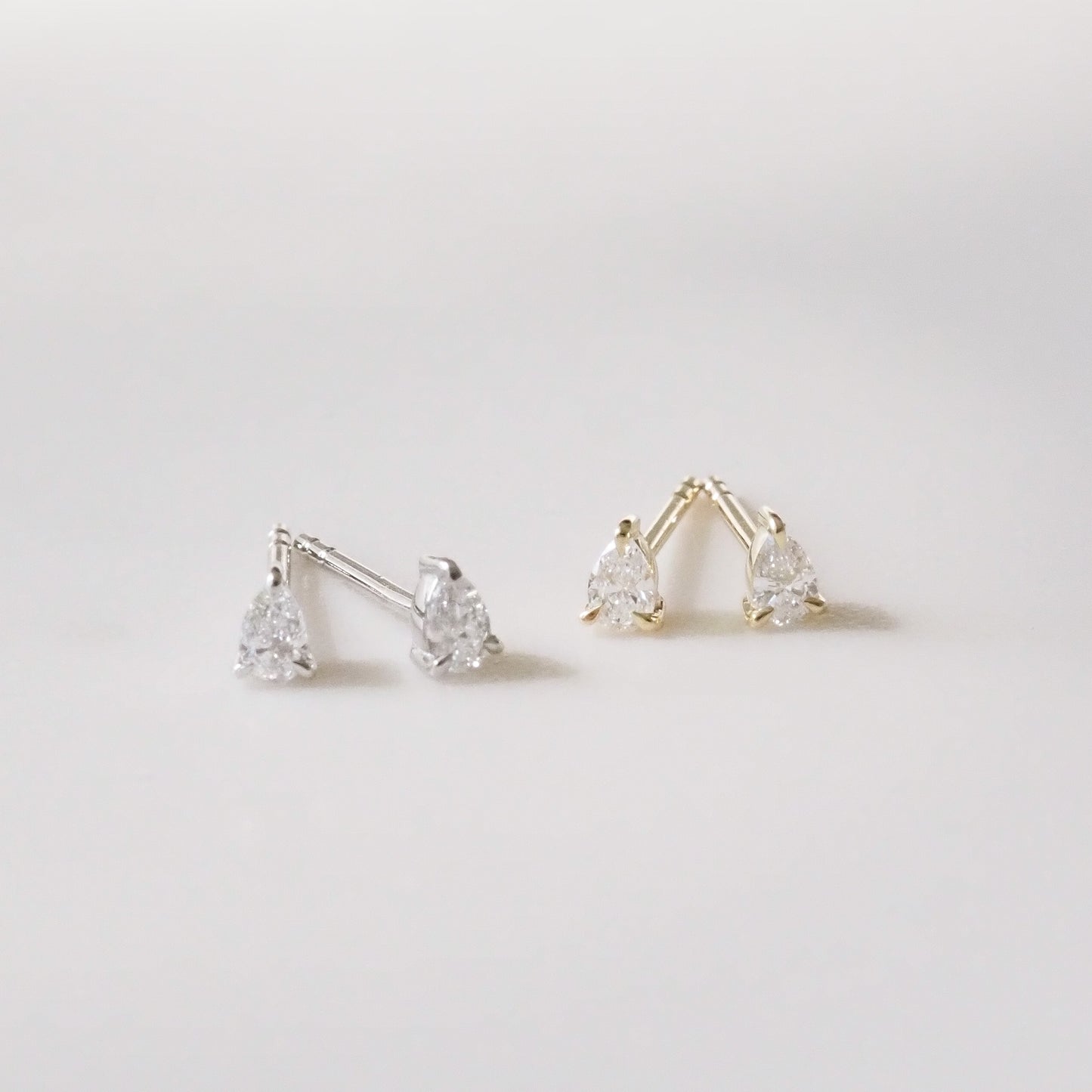 Pair of gold and silver pear-shaped earrings on a light gray background
