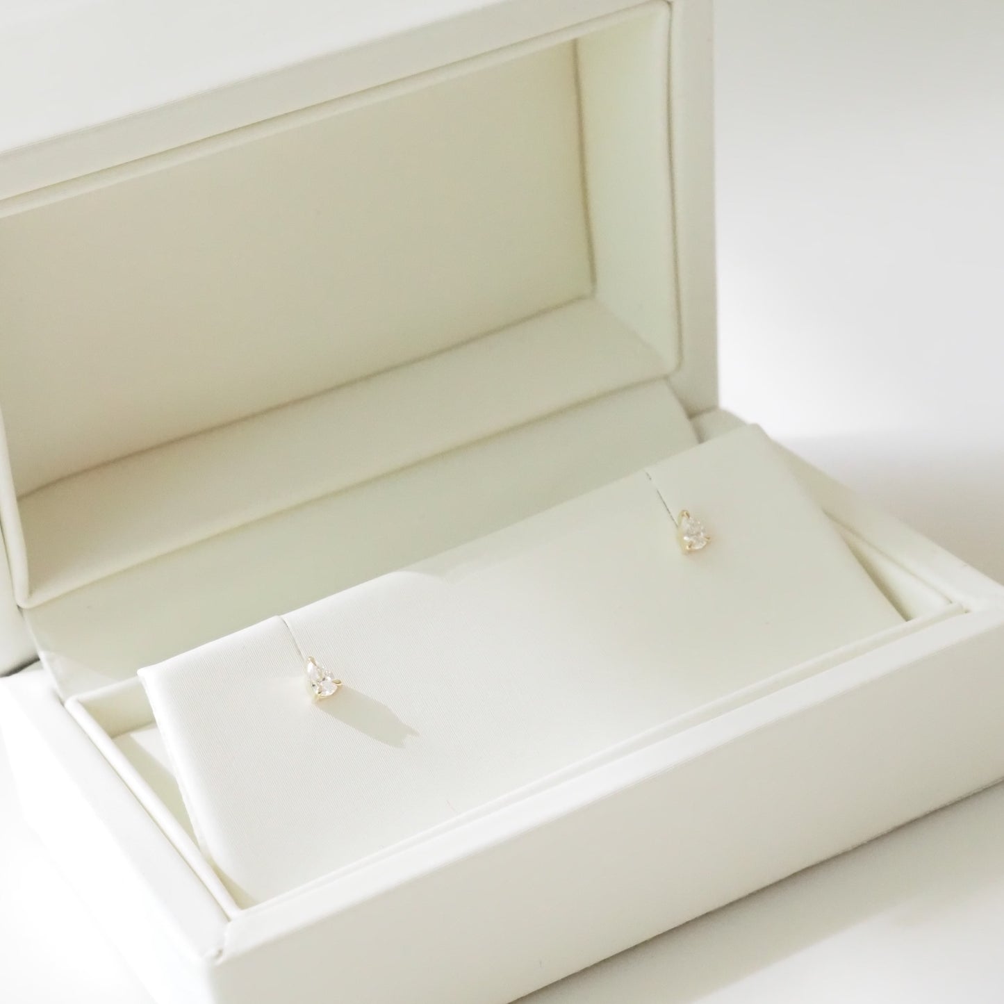 Open beige jewelry box with pear earrings inside on a white background