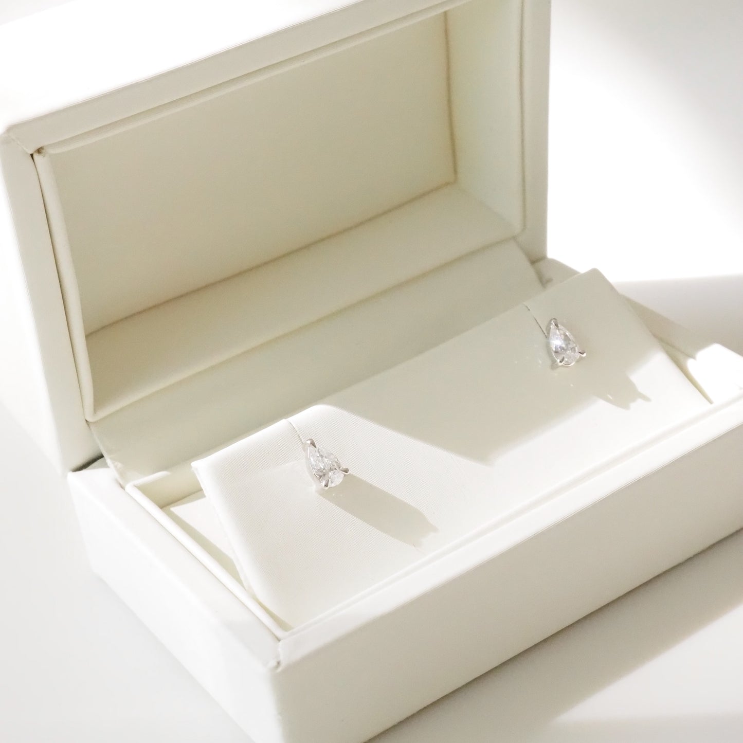 Open beige jewelry box with pear diamond earrings inside on a white background