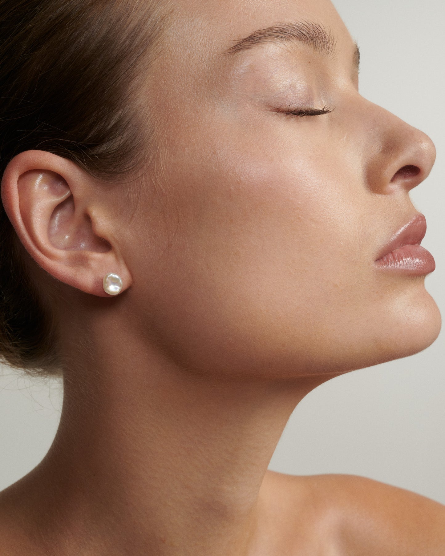 Close-up of a woman's face with a pearl earring on a neutral background