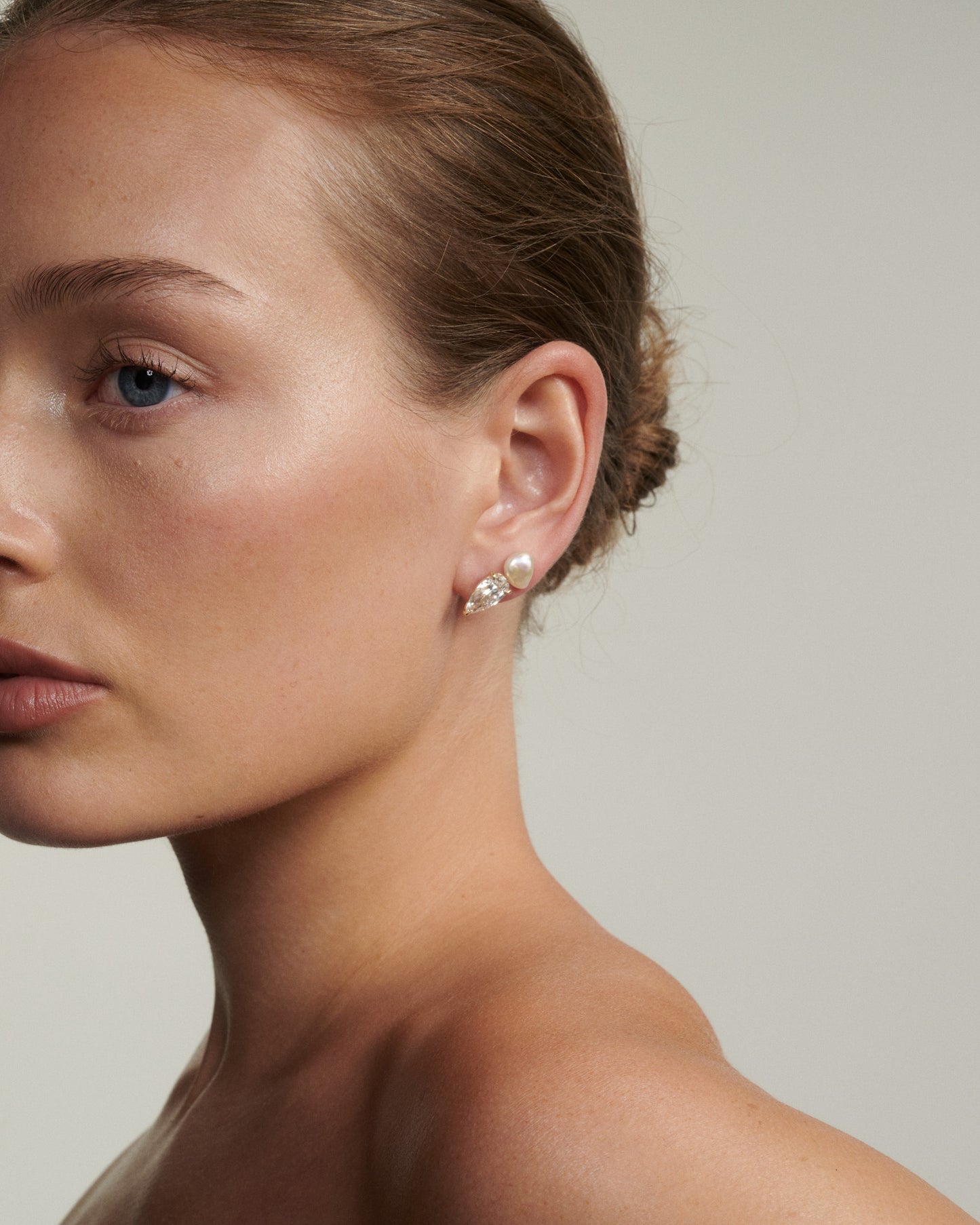 Close-up of a woman wearing diamond and pearl earrings against a neutral background [text overlay: Andrea wears the Pearl Studs & Nouve Studs] 