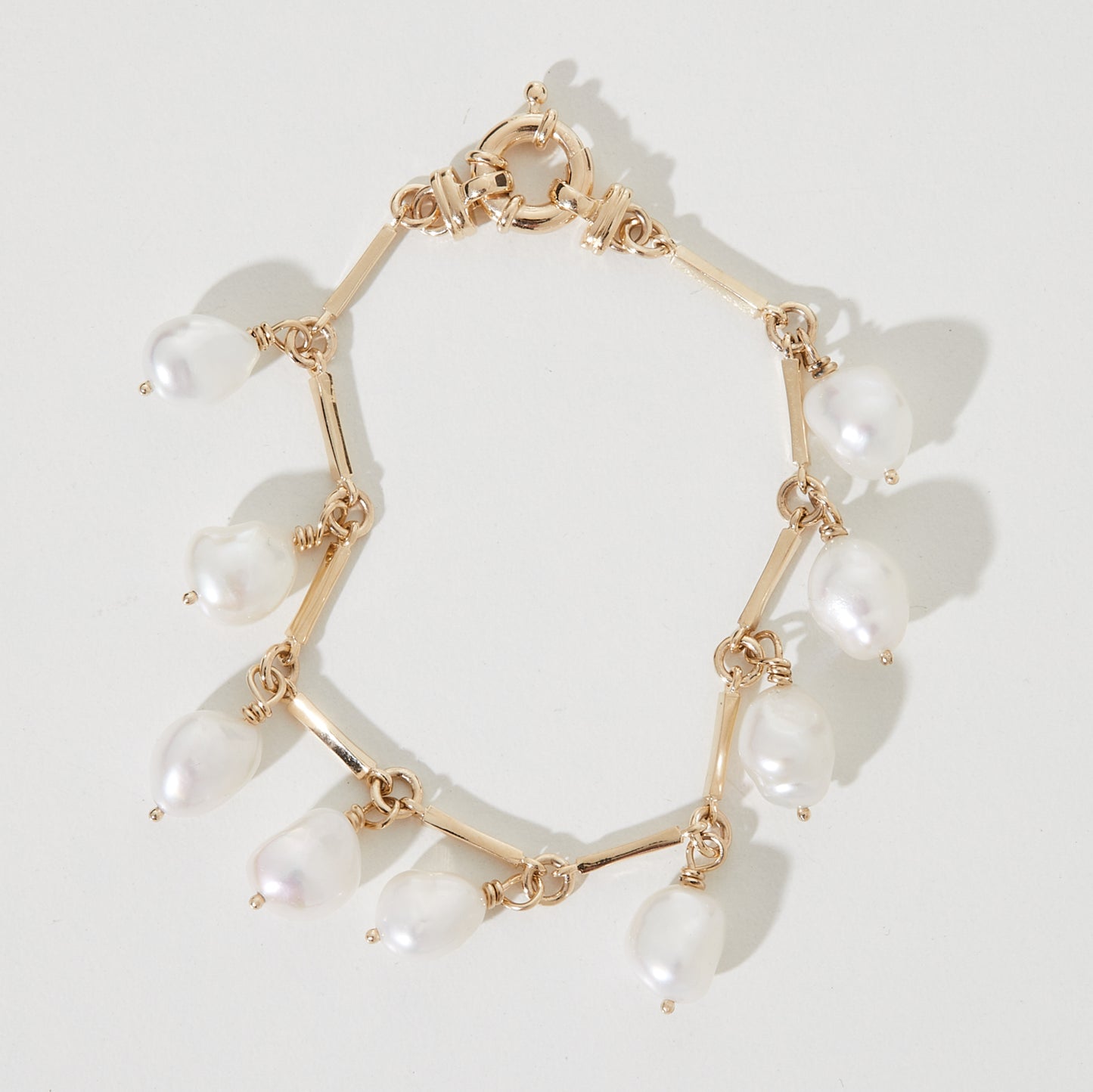 Gold bracelet with pear-shaped white pearls evenly spaced around it, casting soft shadows on a light background.